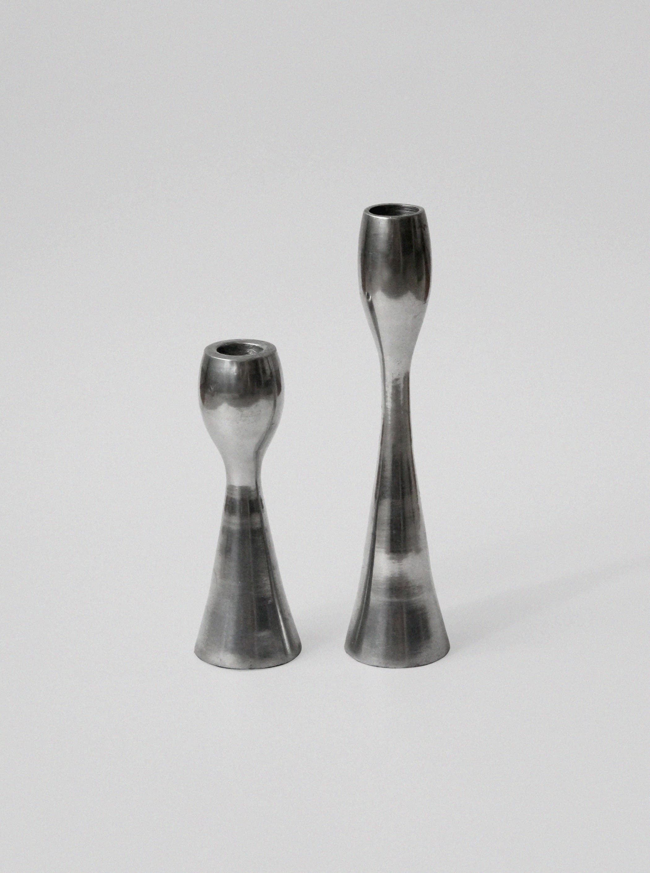 Two polished aluminum candleholders with sleek hourglass silhouettes