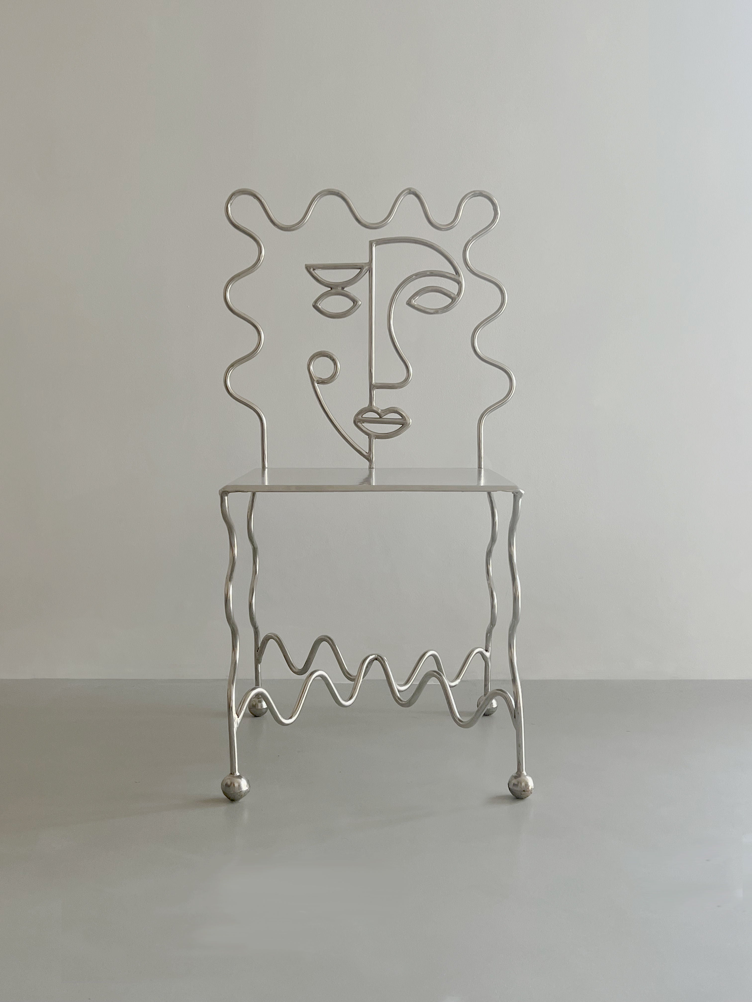 The 'M. Dupont' Chair by Zerom Studio features a modern, wavy silver design with an abstract face and wave-patterned legs. Part of a limited edition series, this collector's item is set against a plain light gray background.