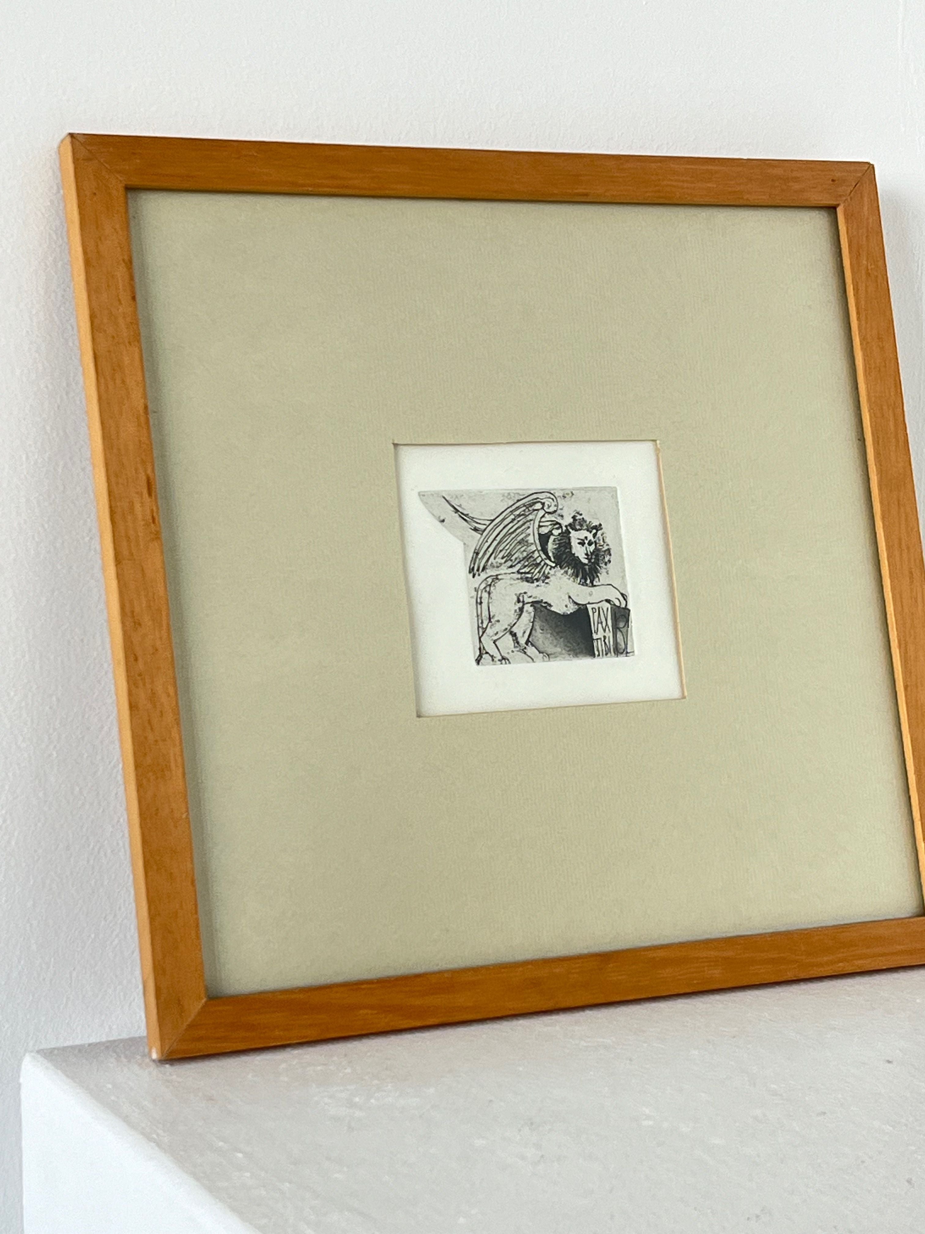 The "Framed And Mounted Hand Illustration" by Porter Studio showcases a detailed depiction of a mythological creature with wings and the body of a lion, enclosed in a small square surrounded by a broader mat border. This intricate illustration in Latin style is encased in an oak frame and elegantly leans against a white wall.