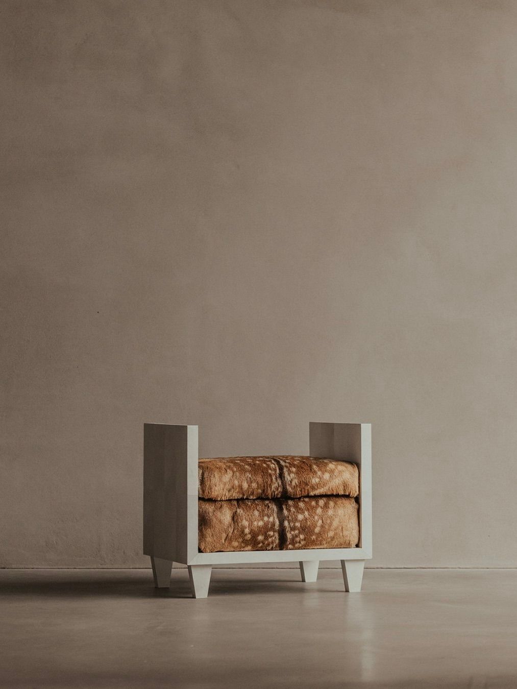 The Sycamore Bench - Parchment Seat by Bicci de' Medici boasts a minimalist design with a wooden frame and brown, textured cushion, inspired by Jean-Michel Frank. Its clean lines and neutral colors complement any plain beige wall and seamless floor effortlessly.