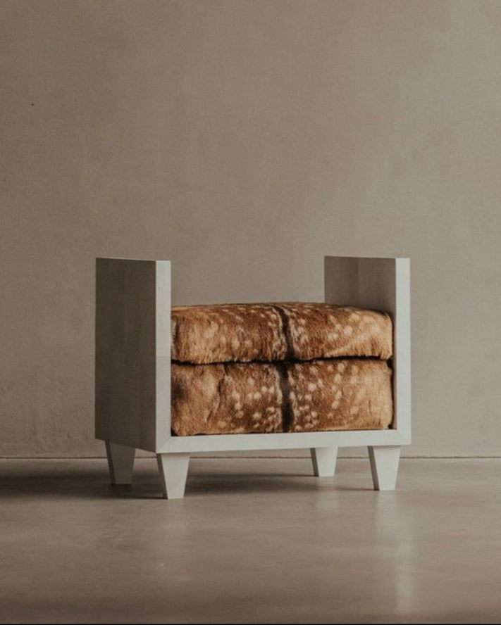 The Sycamore Bench - Parchment Seat by Bicci de' Medici boasts a minimalist design with a wooden frame and brown, textured cushion, inspired by Jean-Michel Frank. Its clean lines and neutral colors complement any plain beige wall and seamless floor effortlessly.