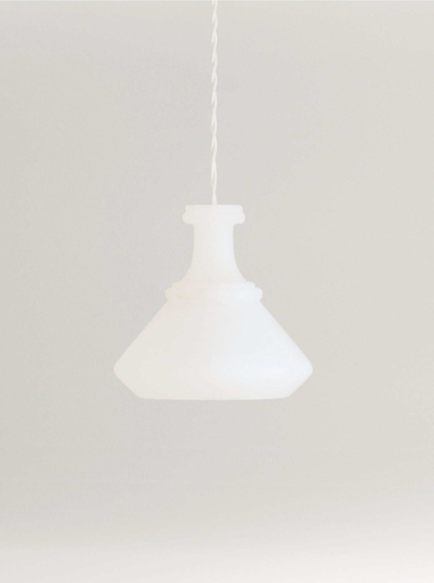 A minimalist image featuring a Dolia Ceiling Light by Marine Breynaert hanging from a ceiling, set against a plain, light gray background for a clean and simplistic aesthetic.