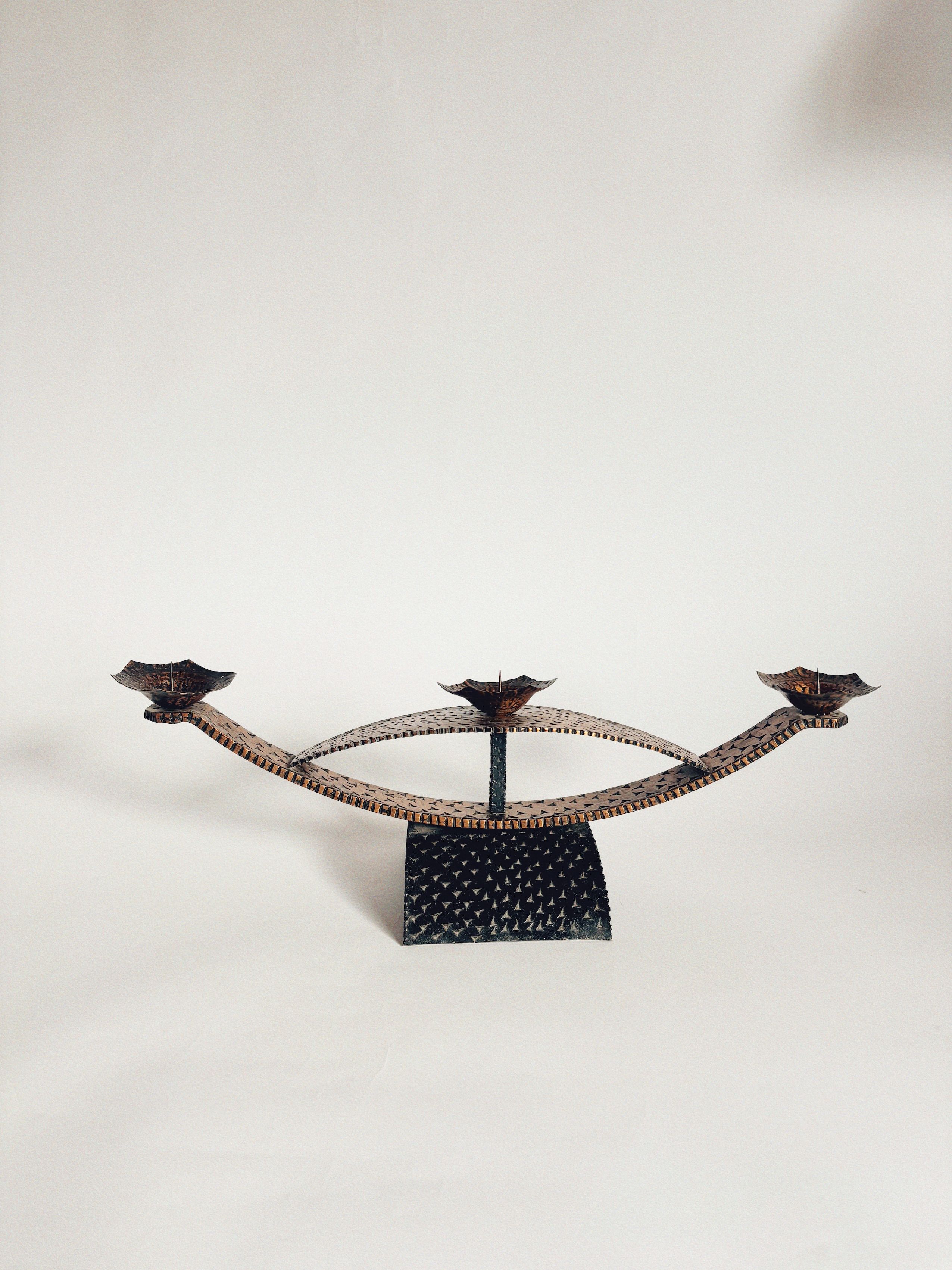 The Huerto Two Tone Metal Candleholders feature three flower-shaped holders on curved arms and a textured base, offering vintage charm in decorative black metal, beautifully set against a plain white background.