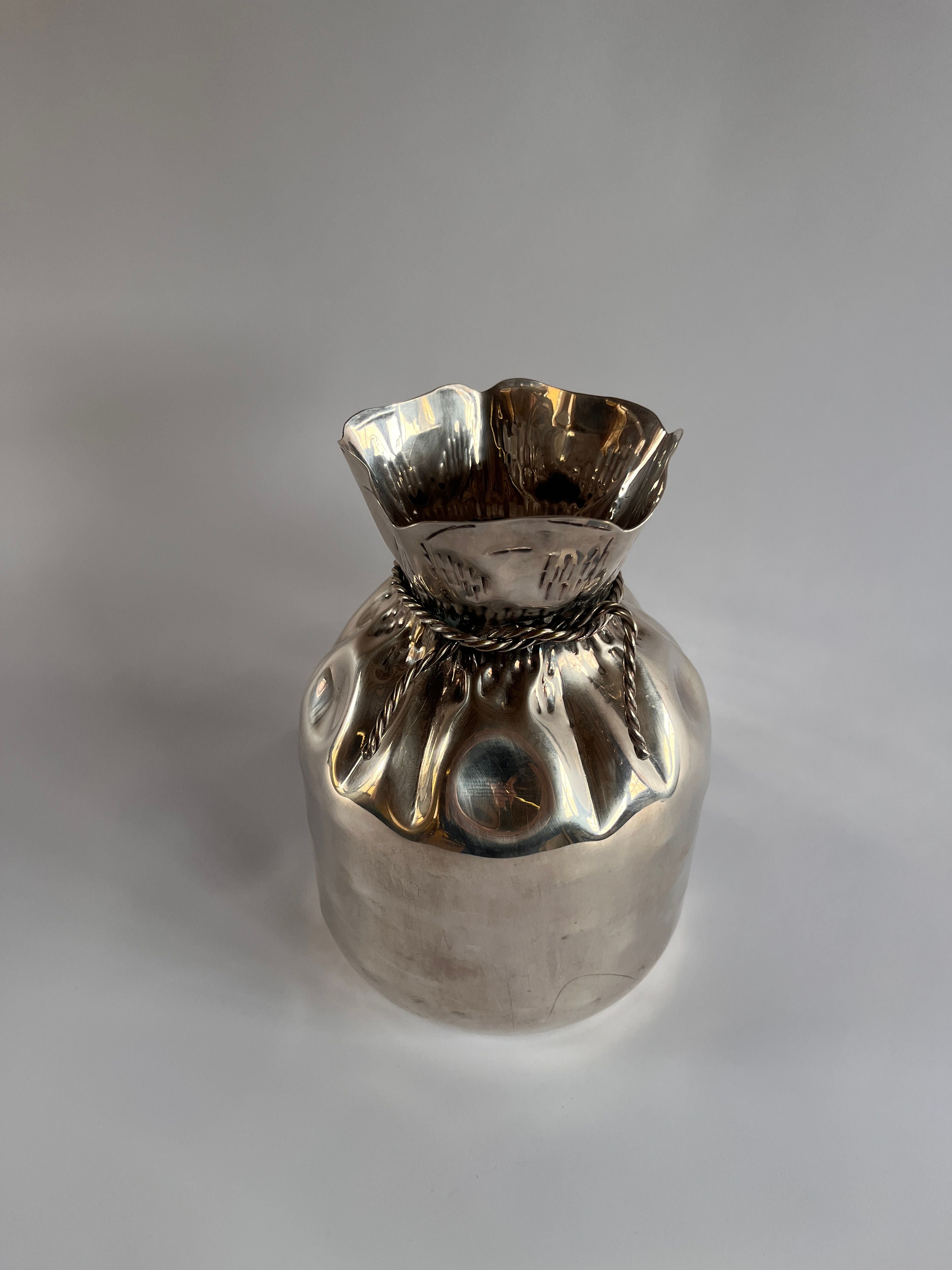 The Silver Plate Vase by Aspreys of London, crafted by Maud Vaughan, features a small metallic design with a ruffled flared top and round base. Its shiny surface gleams against a neutral backdrop, evoking the elegance of vintage silver-plated pieces.