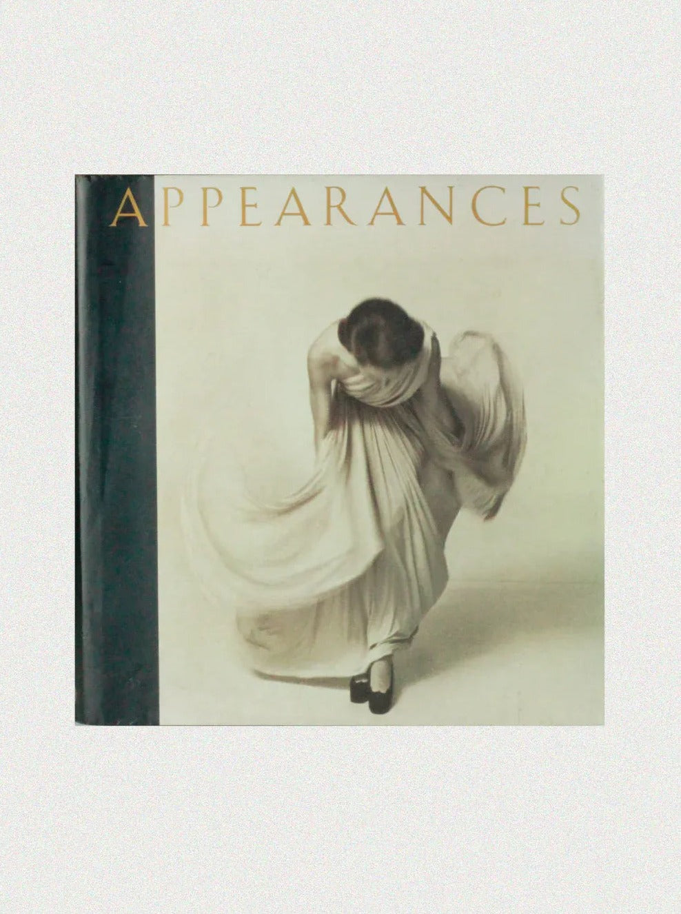 The book cover of "Appearances by Mark Holborn - Vintage Book," available from Boga Avante Shop, features a sepia-toned photograph of a person gracefully draped in a flowing dress, reminiscent of vintage fashion photography. The title "APPEARANCES" is printed in large, elegant uppercase letters at the top. Curated by Martin Harrison, the spine of the book is black.