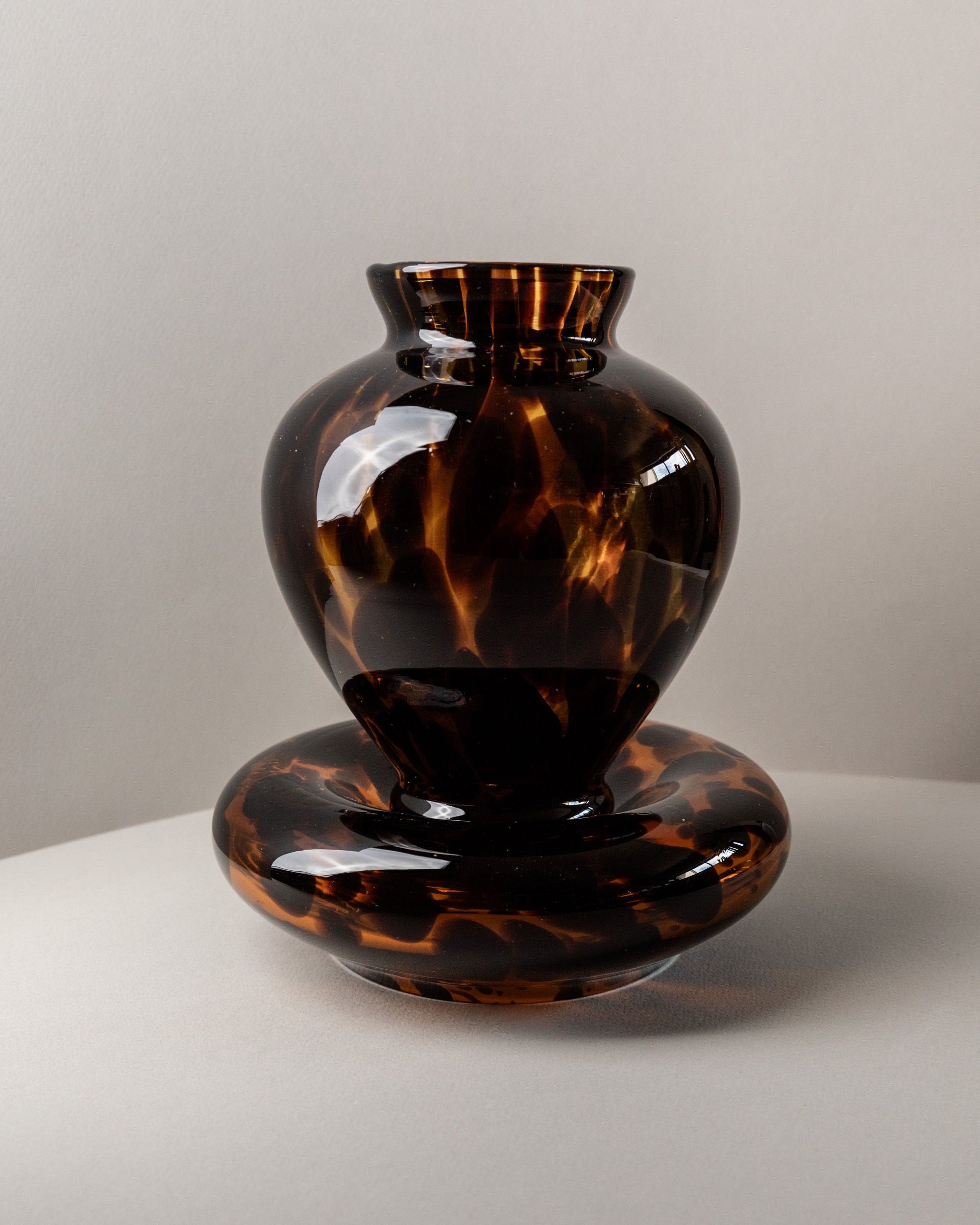 A glossy, dark brown Set of Murano Glass Vase and Bowl - Tortoise by Bottega Jacobs (Italy, 80s) featuring an abstract tortoise shell pattern sits on a light surface with a pale background—true Italian glass artistry.