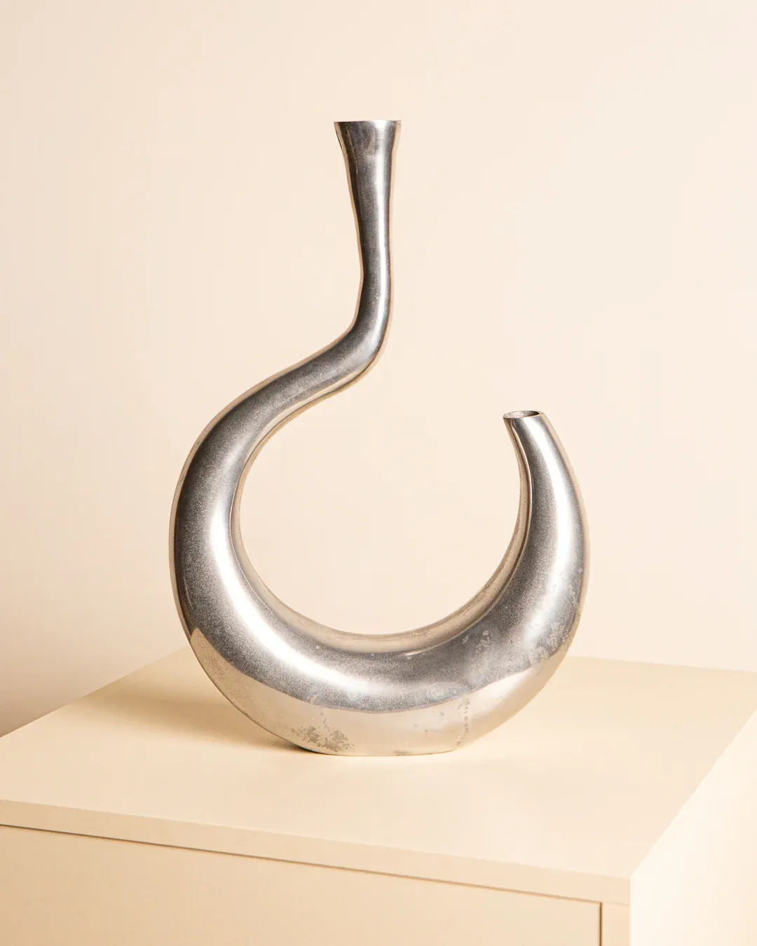 The Vase "Ondule" in Aluminum 80's by Treaptyque features a sleek, modern asymmetrical design, resting on a light surface against a beige backdrop, capturing the chic essence of Milan design.