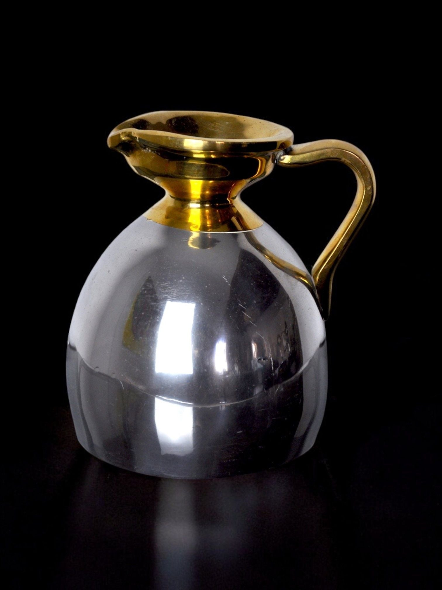 Placing the Brutalist Jar by Art3 against a black backdrop, this piece from Malamar Studio features a reflective silver and gold body. With an elegant gold handle and spout, it exudes sophistication, capturing the essence of modern design artistry from Spain in 1980.