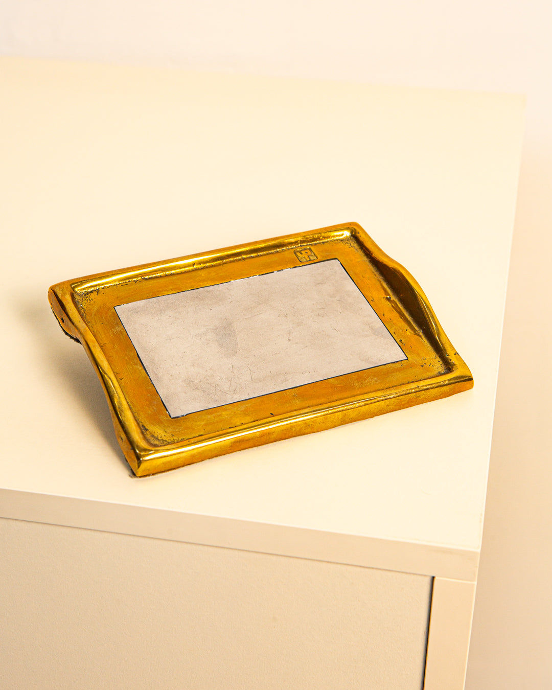 The Treaptyque Vide-poches by David Marshall 80's features a rectangular brass-and-silver design with a flat gray center and raised edges, displayed on a light table against a plain background, reflecting ‘80s style.