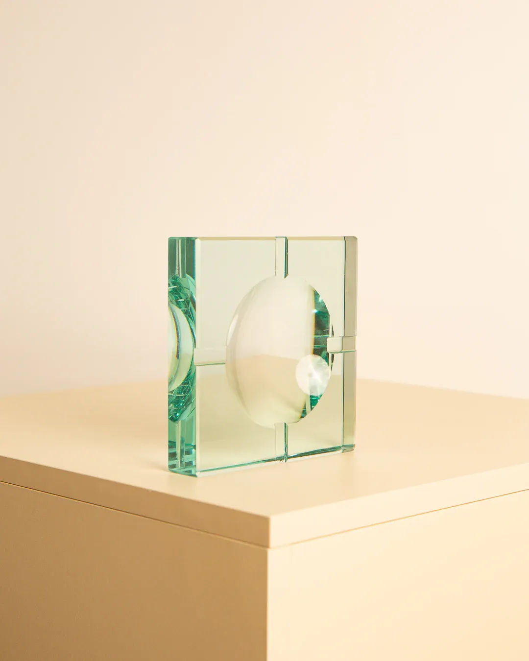 A clear glass decorative sculpture with geometric and spherical elements sits atop a beige surface against a light background. Reminiscent of the classic Glass ashtray by Fontana Arte 70's, the sculpture features a central round shape encased within angular segments, creating an elegant and modern Italian design aesthetic by Treaptyque.