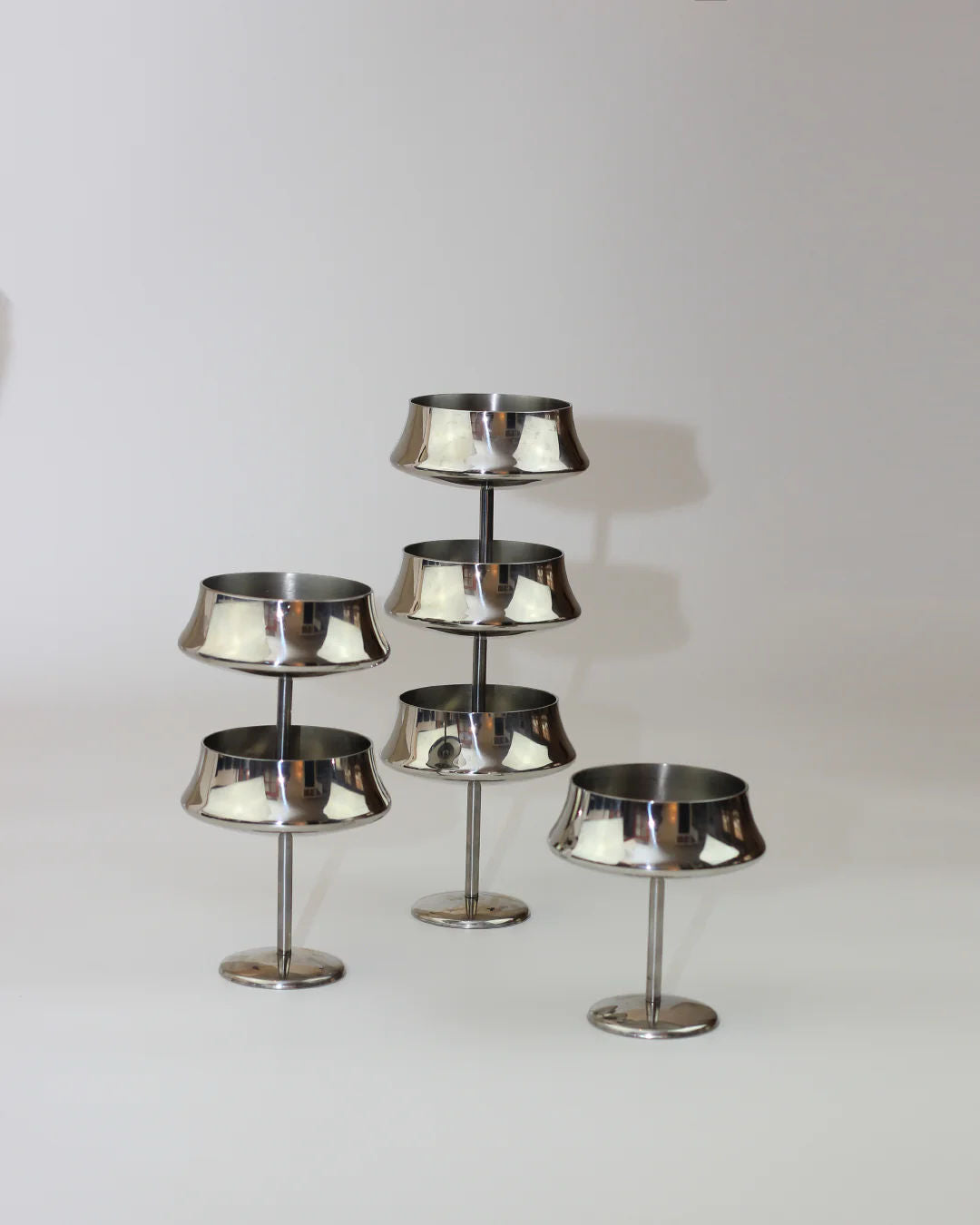 Six stainless steel cups from Boga Avante Shop are arranged in a staggered formation against a light background. Perfect for serving fruits or desserts, each cup features a round base and a shallow, wide bowl.