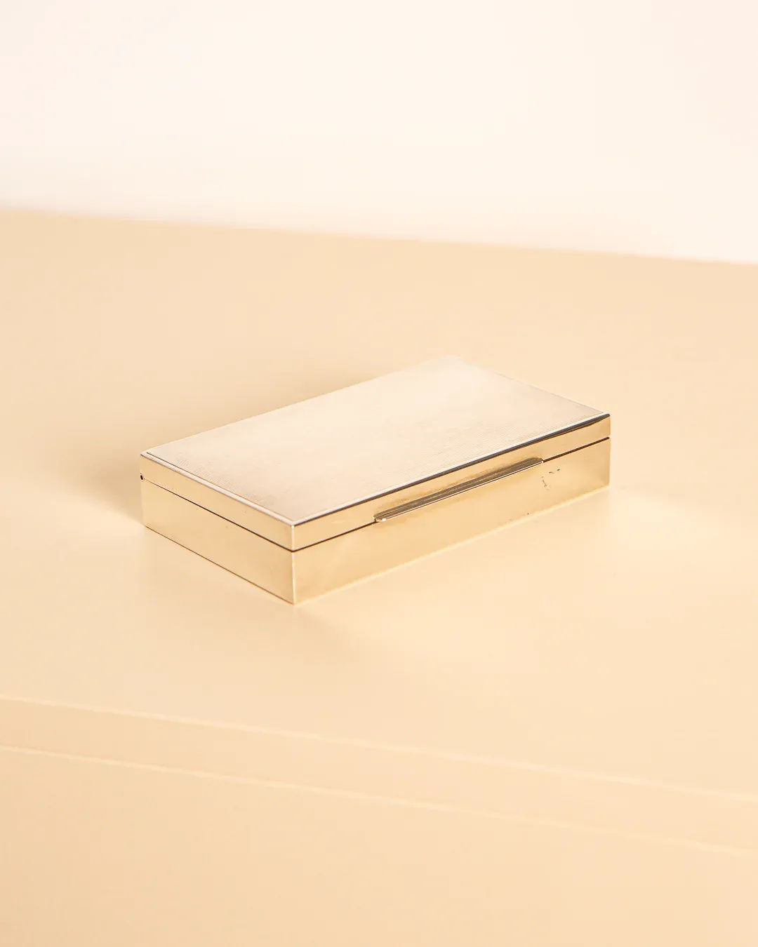 A rectangular silver and wood box from Treaptyque, featuring a sleek and minimalist design evocative of 1960s Italy, rests on a beige surface against a light background.