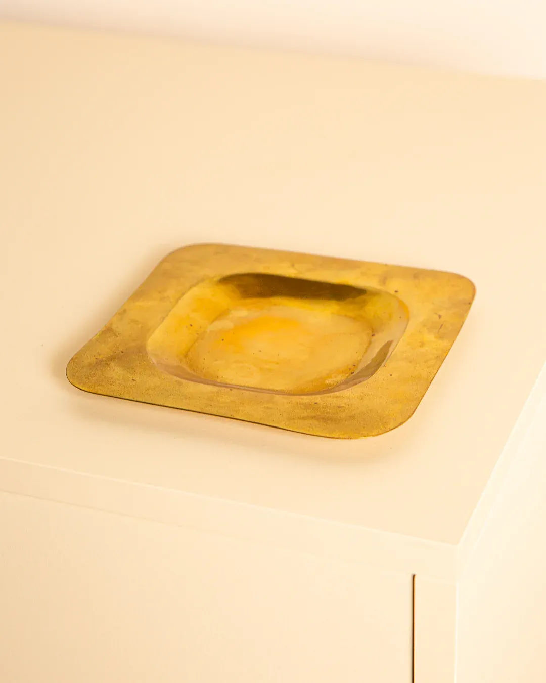 A vintage decor piece, the Italian Patinated Brass Vide-poches 60's by Treaptyque rests on a cream surface. Its metallic finish reflects light, highlighting its smooth texture and patinated look.