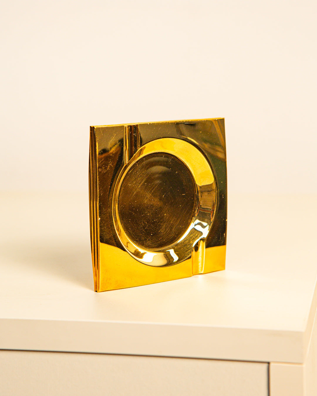 The Brass Ashtray by Francois Gross 60's from Treaptyque features a shiny, square brass design with a circular indentation and cigarette notch—perfect for adding a touch of 60s style to any space.