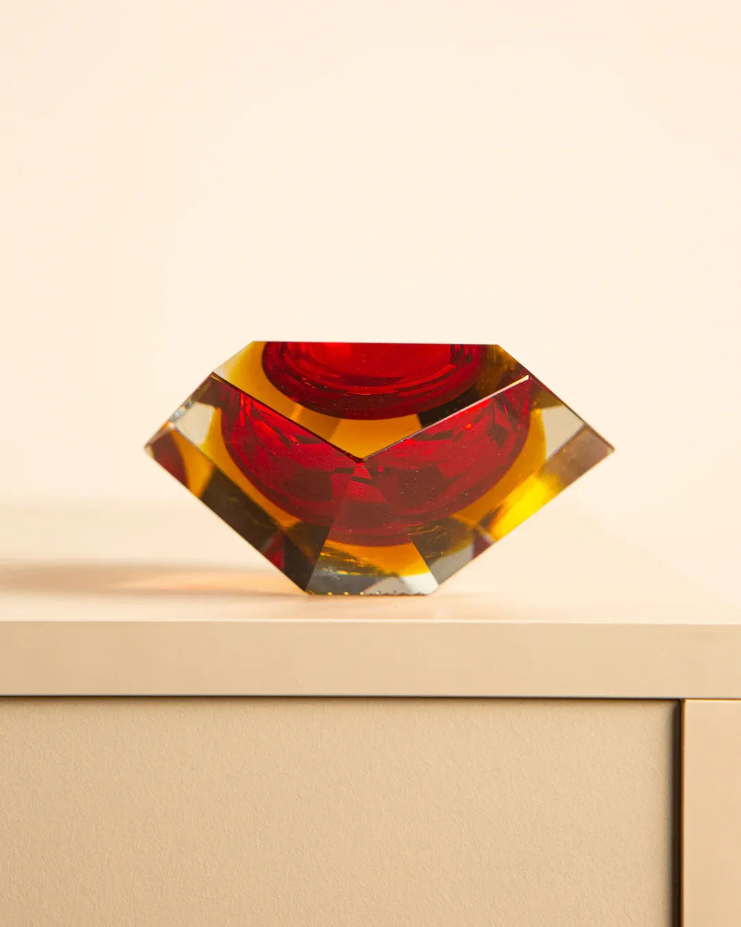 The Treaptyque 'Diamant' Ashtray Murano by Flavio Poli for Seguso 60’s features geometric glass with a red center and amber edges on a light surface, reflecting brilliantly to create a striking contrast against a plain background.