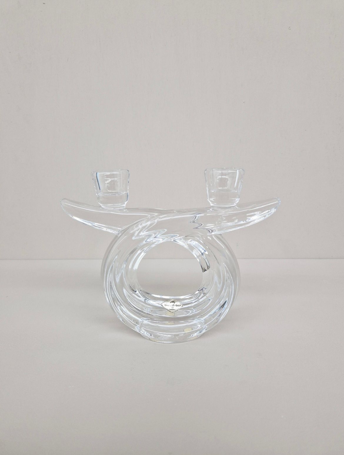 The Crystal Candle Holder 1960s by Flock Studio features a clear glass design with a sculptural, twisted circular shape, reflecting mid-century elegance with dual top candle slots, set against a plain light background.