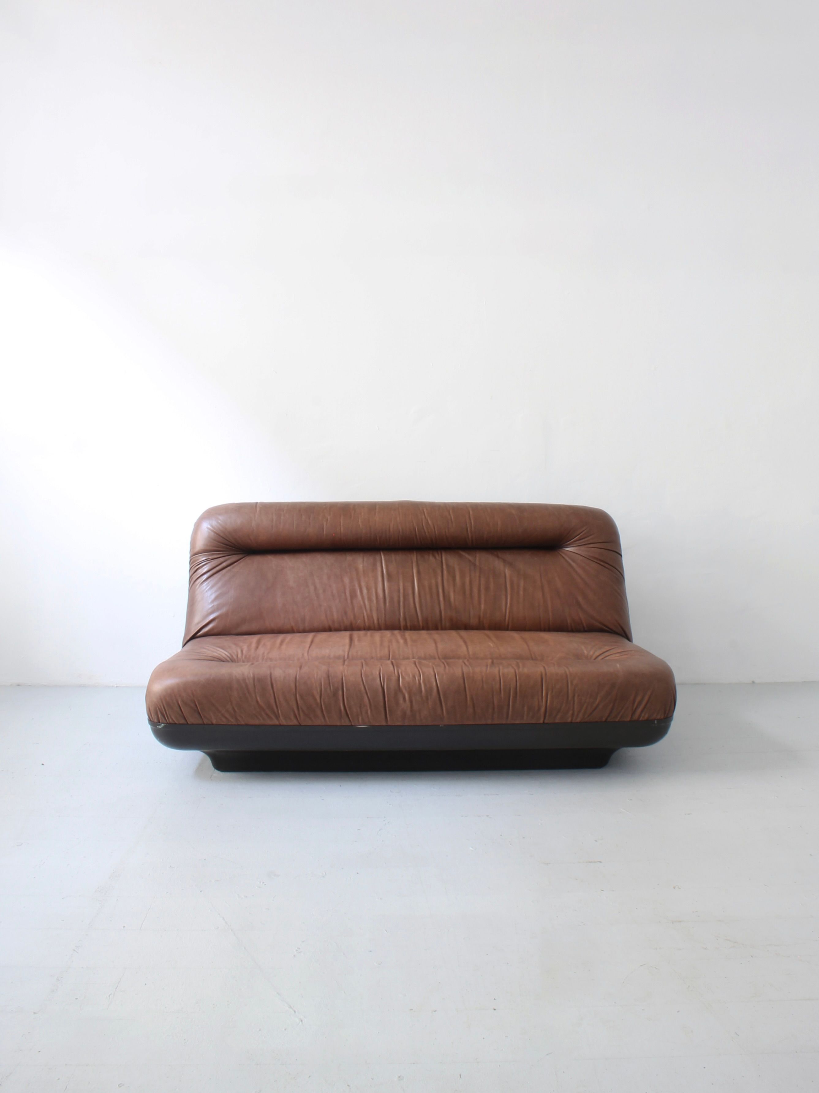 Afterhour Furniture's "Leather Sofa by Gerd Lange," featuring a tufted backrest and no visible legs, enhances the minimalistic room with its mid-century modern style, evoking 70s aesthetics.