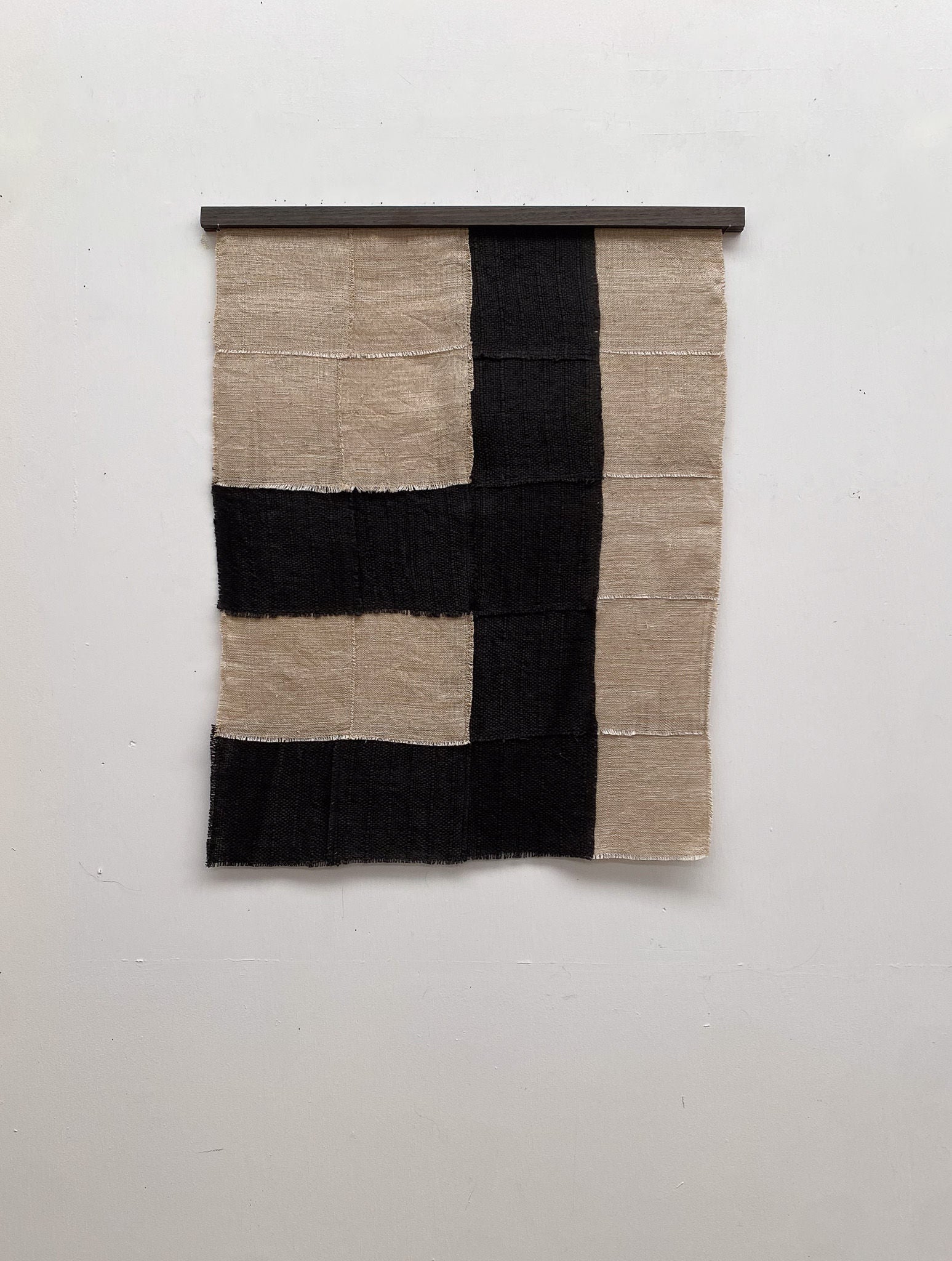 The "Paths" textile wall hanging by Sundance Studio is crafted from antique cotton, showcasing a checkerboard pattern with alternating large beige and black squares and a distinct black cross extending both vertically and horizontally.