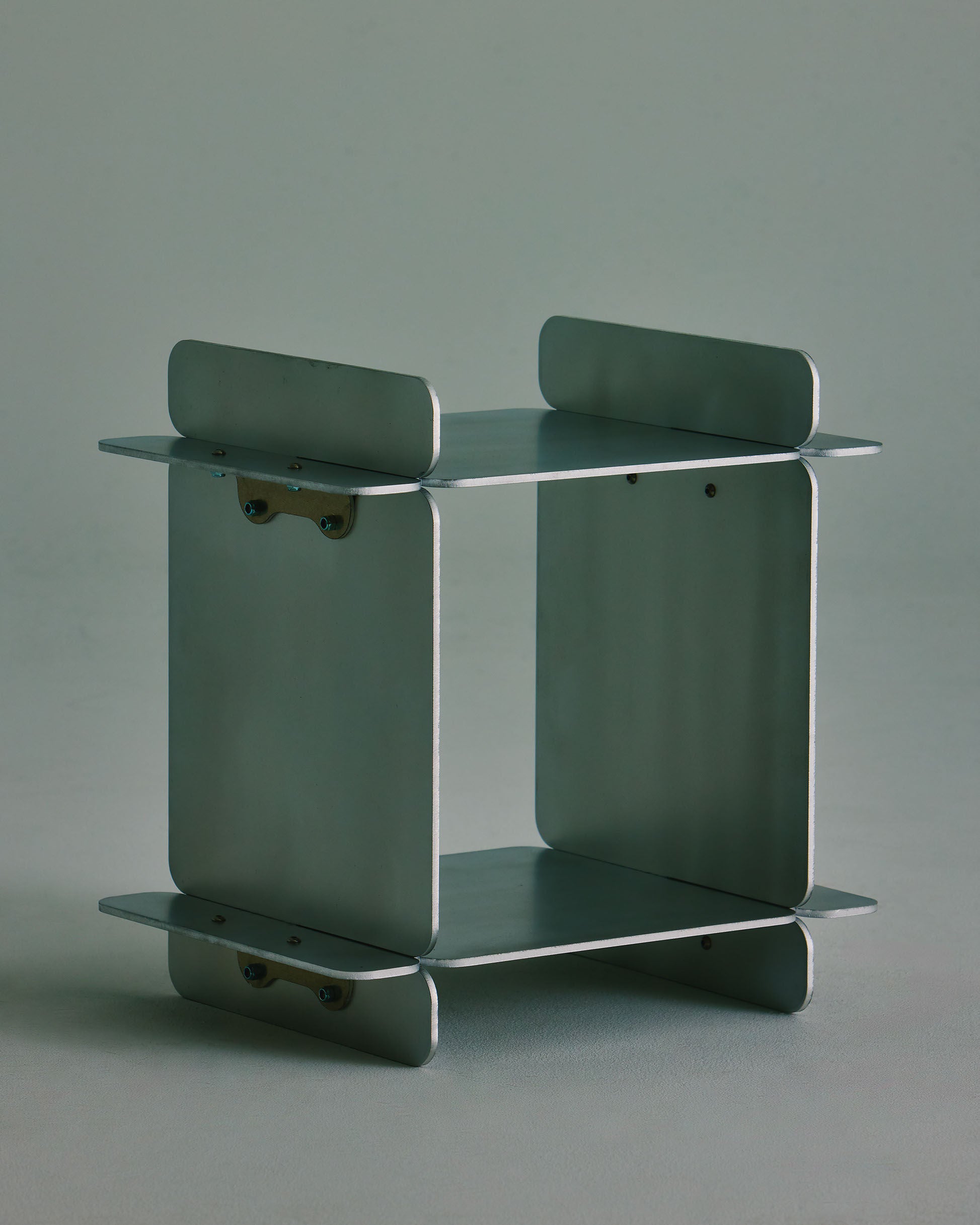 The Side Table by LESORR features flat, rectangular metallic panels forming the top, bottom, and sides, joined by visible brackets for a subtle brutalist flair—all set against a neutral backdrop.