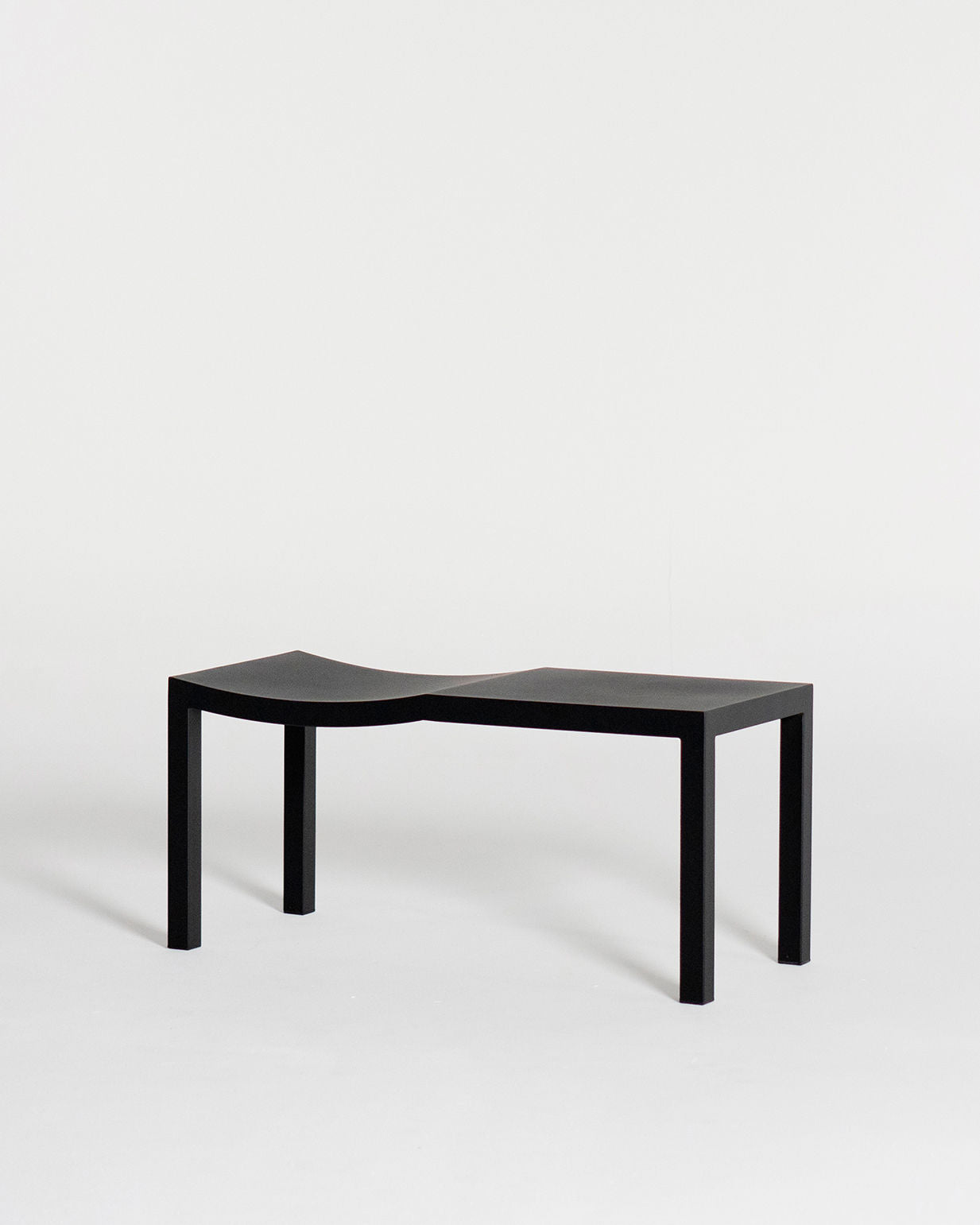 The "Bis" bench by Andre Grippi is a minimalist black seat with four straight legs and a slightly concave surface for two, shown against a plain white background.