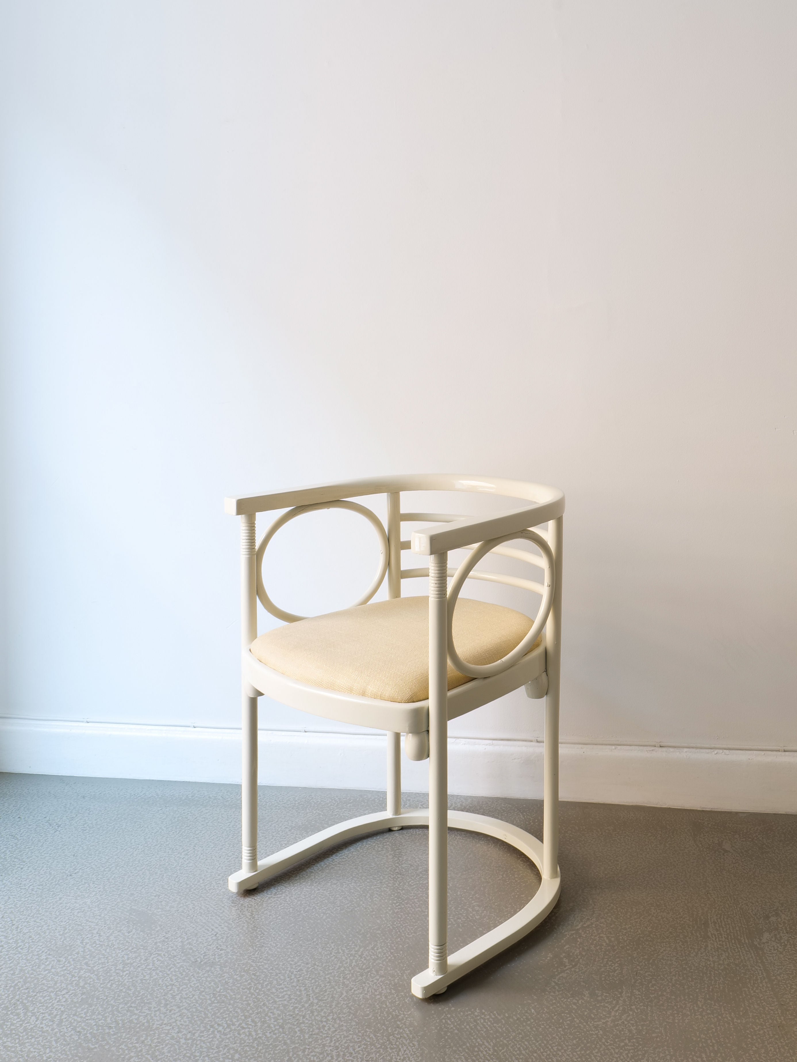 A Thonet Bentwood Chair by Josef Hoffman from the Collection apart brand, featuring a modern design with a circular backrest and upholstered seat in beige, rests on a light gray floor against a plain white wall.