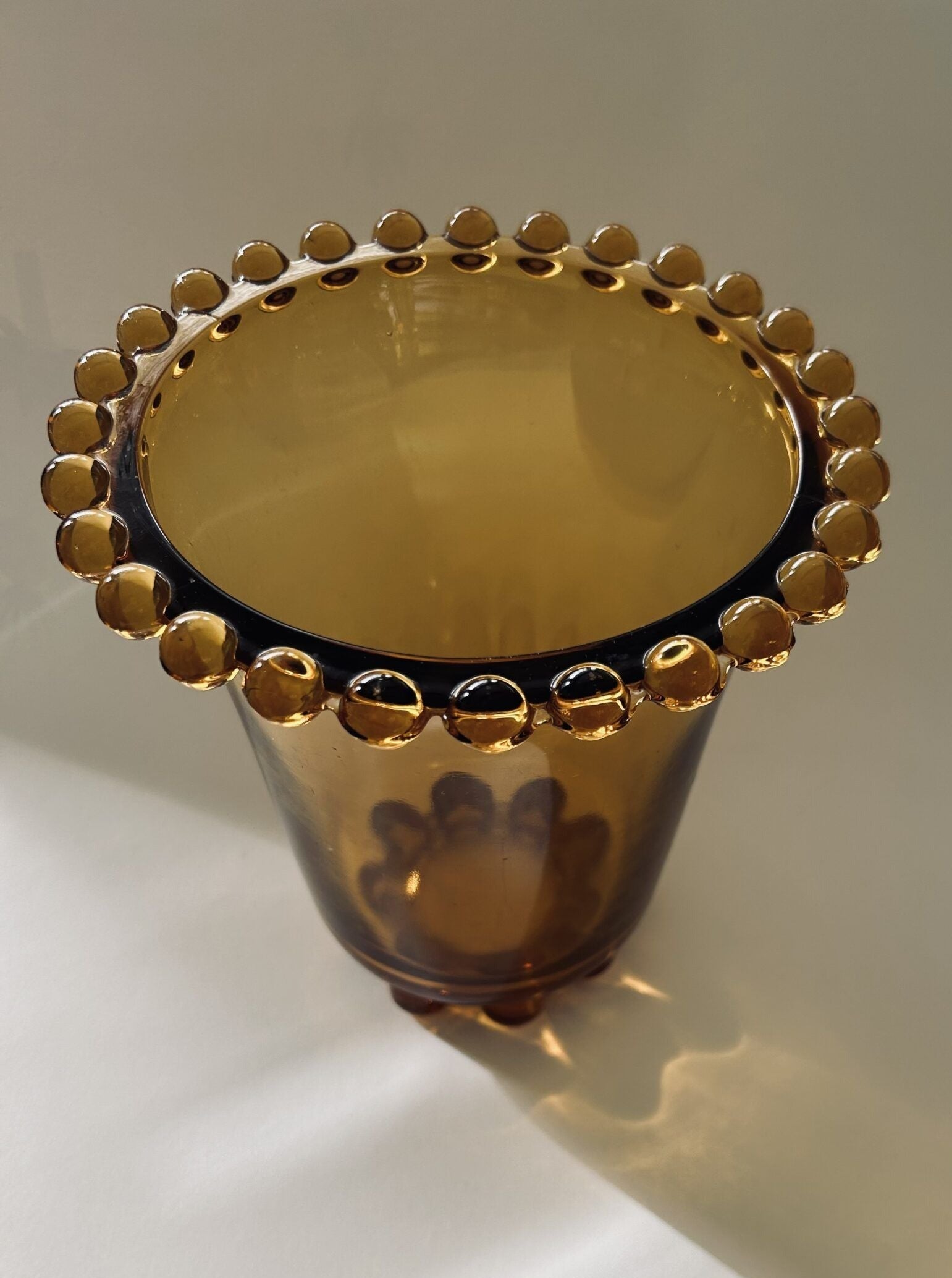 The Art Deco Amber Glass Vase by Rudolf Schrotter from Flock Studio, featuring a scalloped edge adorned with round beads, casts a soft shadow on a light surface.
