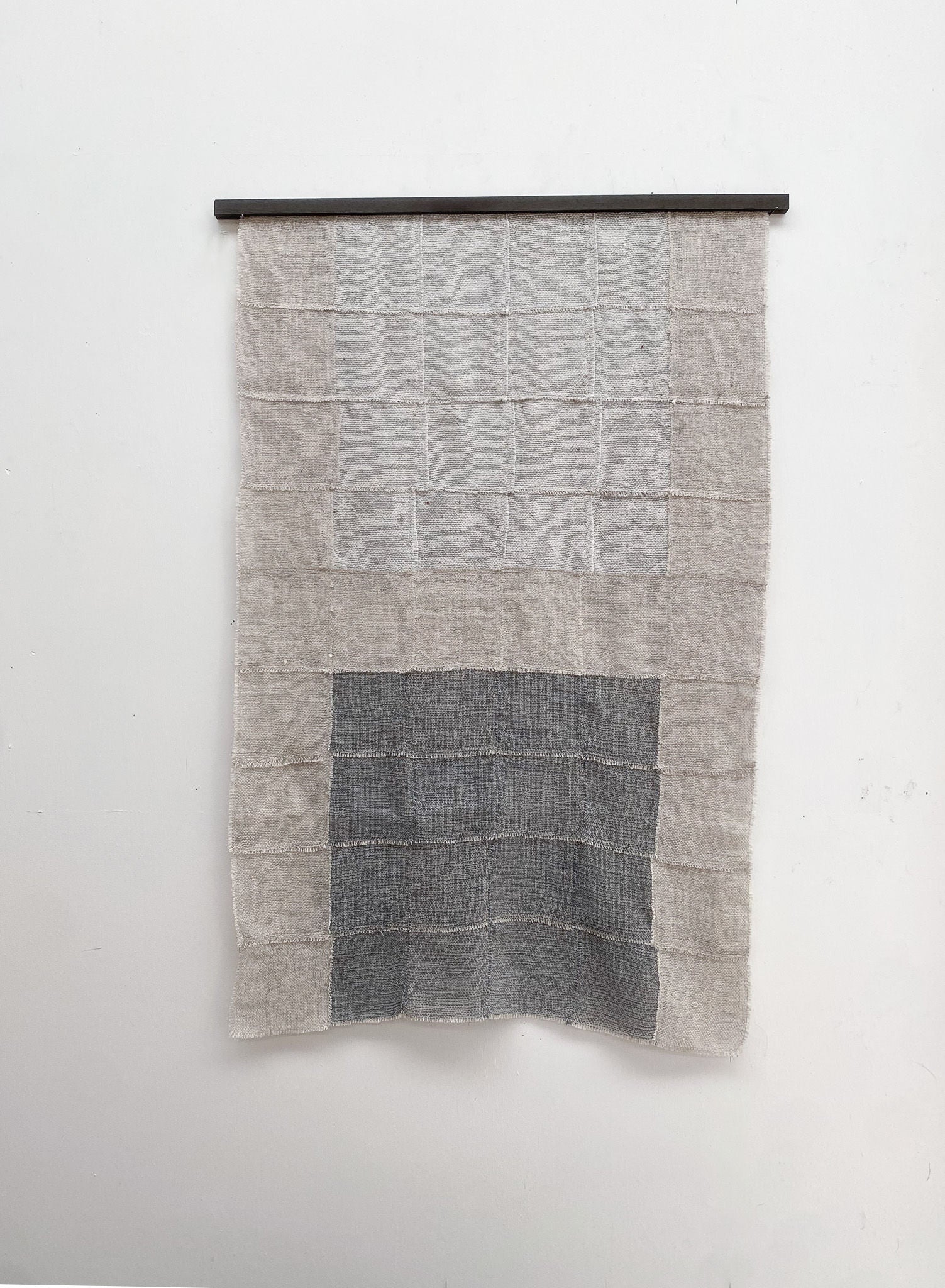 The "Blue Sky" Artwork by Sundance Studio is a woven wool-cotton wall hanging with a grid pattern and a prominent gray rectangle at the lower center, displayed on a rod against a plain white wall.