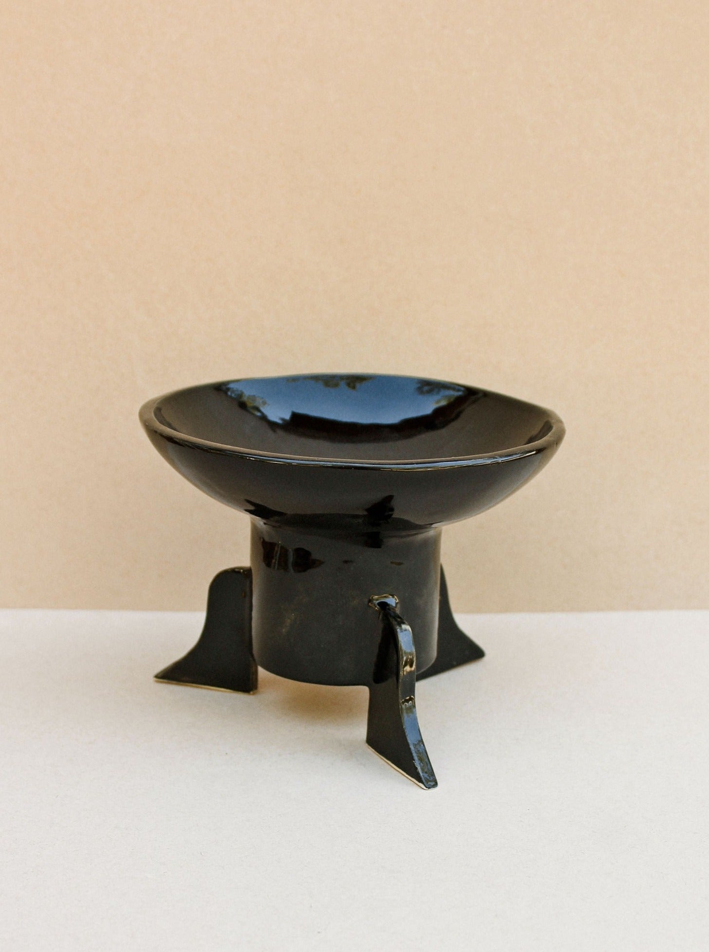 The Dolores Bowl/Catch All (Negro) by Casa Veronica is a glossy black ceramic piece with a wide rim and three angled legs, shown against a neutral beige background.