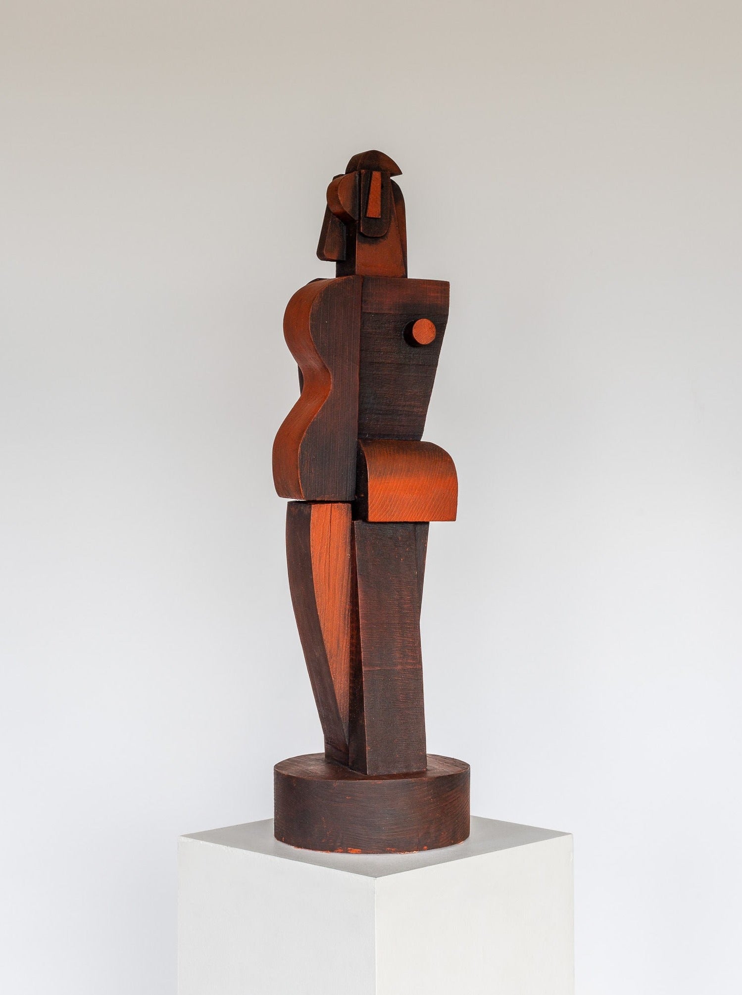 A Cubist Sculpture from Spigel, featuring abstract, geometric shapes, is displayed on a white pedestal. The piece consists of interlocking segments with a combination of curved and angular forms, creating a figure that hints at cubism and remains highly stylized and modern.