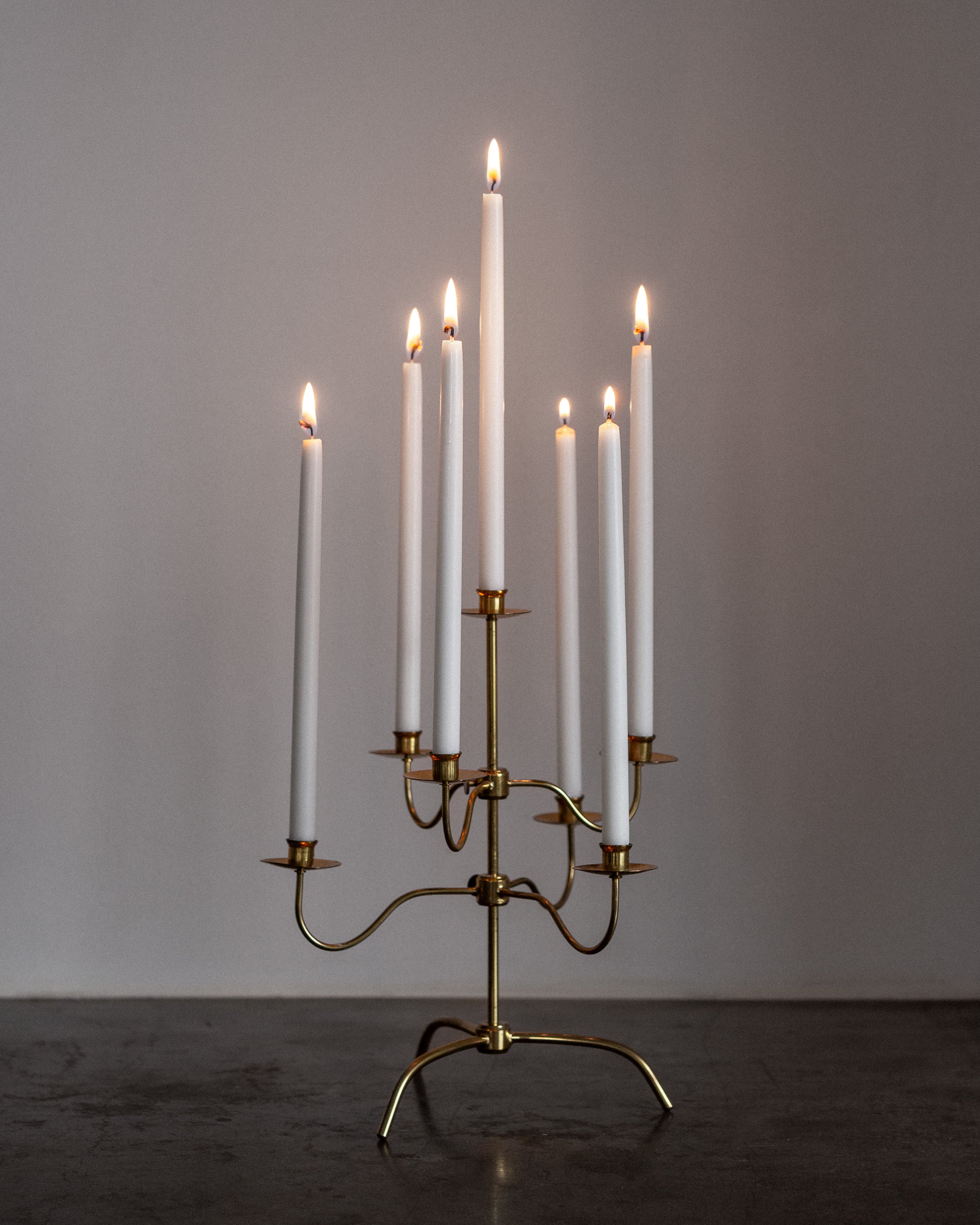 A stunning Scandinavian Modern touch is reflected in the Swedish Mid-Century Brass Candelabra by Spigel. Featuring eight white candles of varying heights, it creates an elegant and symmetrical arrangement against a plain gray background, reminiscent of Josef Frank's design.