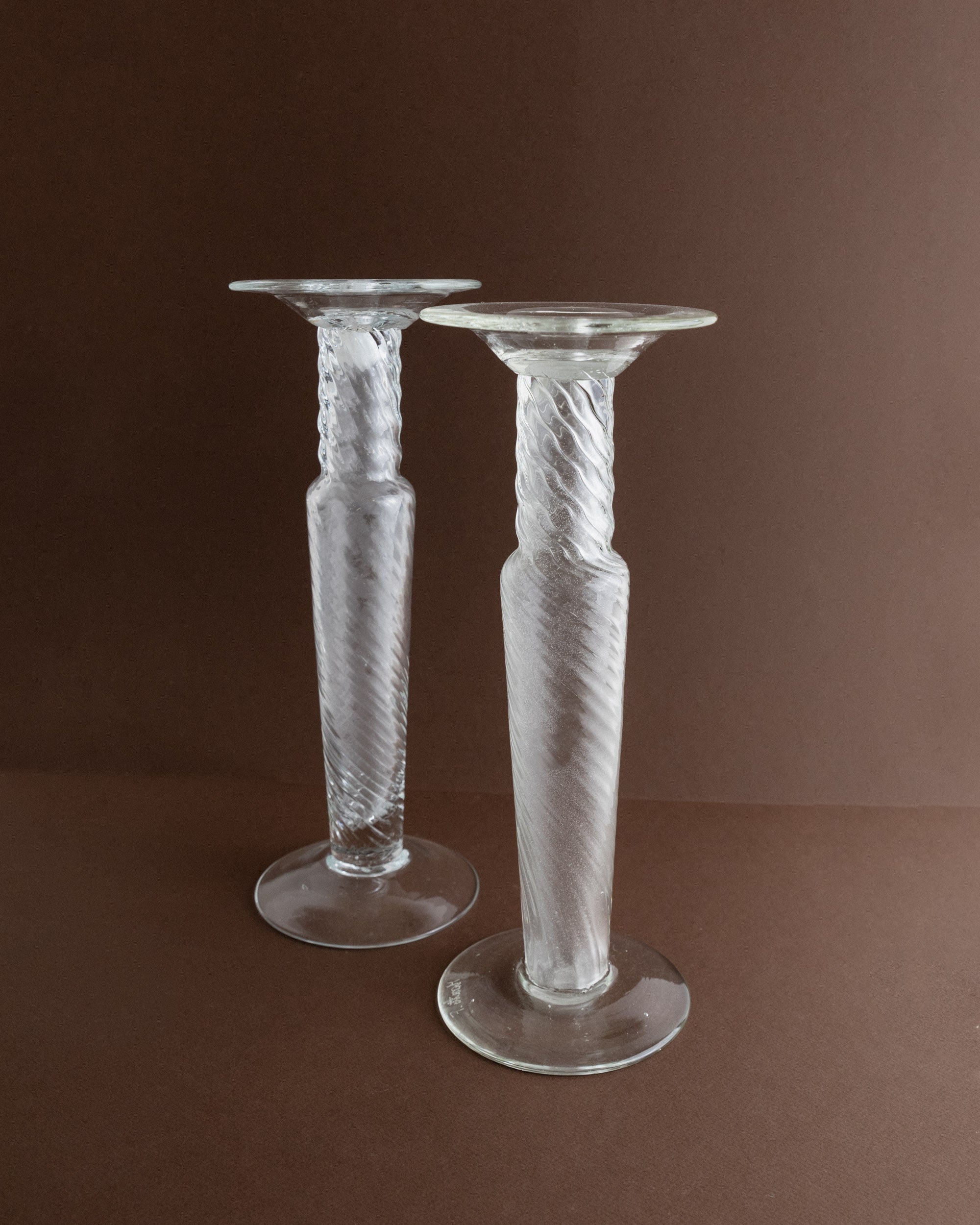 The Franco Moretti Candleholders 60s by Bottega Jacobs stand on a brown surface, featuring a clear glass twisted design. Reminiscent of vintage Murano artistry, they have wide bases and flared tops for an elegant, symmetrical look.