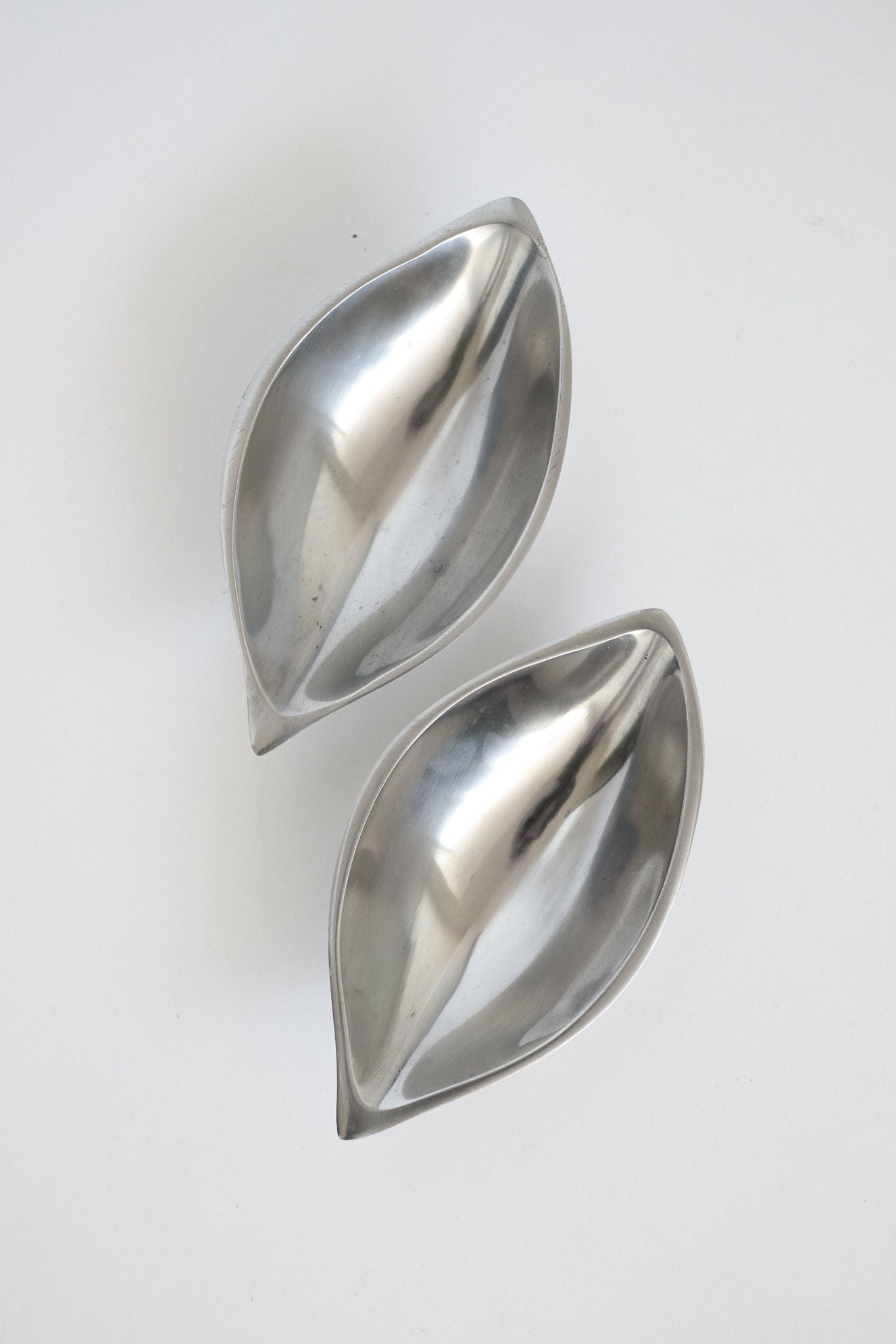 Two polished silver leaf-shaped serving dishes on white background