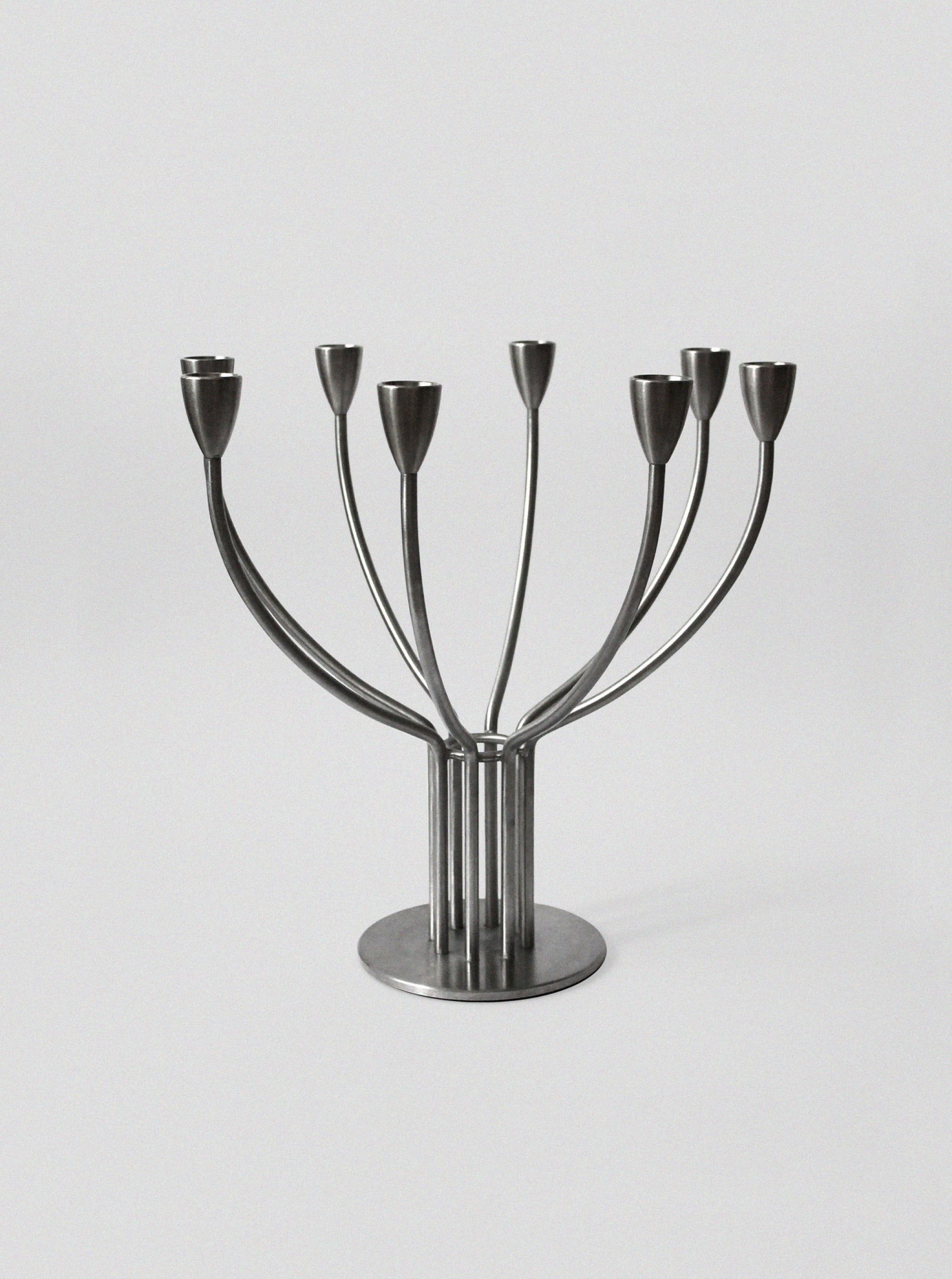 The Brushed Metal Swedish Candelholder by Vintage Stories features seven curved arms and a round base in a minimalist Scandinavian design, perfect for modern décor.