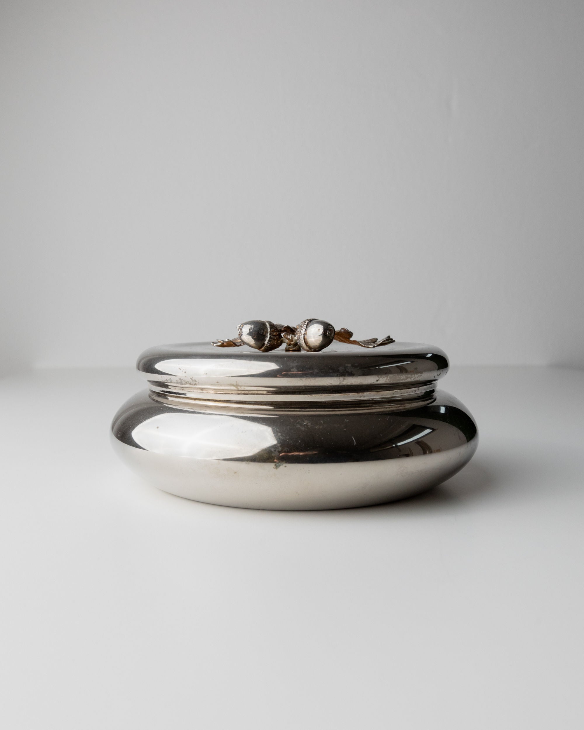 A Silver-plated Box from 1950s Italy by Bottega Jacobs sits on a white background, featuring a smooth, shiny surface with a metallic acorn handle topped by two pearl-like accents.