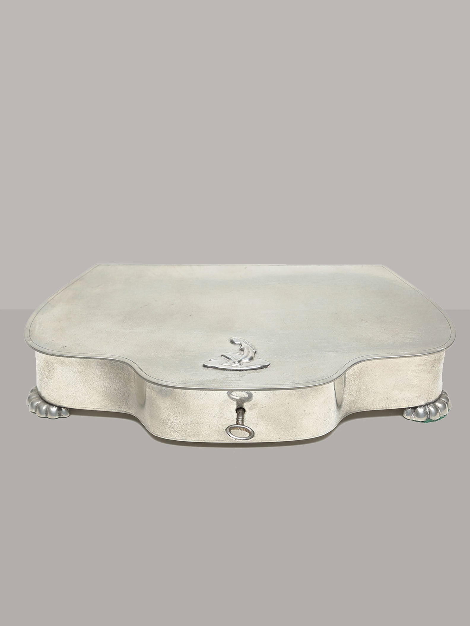 A silver jewelry box from the 1930s by GAB, with a rectangular shape, rounded edges, and a small decorative handle. Its top features engraved designs reminiscent of the Swedish Grace tin box. In excellent condition, it rests on four ornate feet against a plain gray background. Brand: RELIC LONDON.