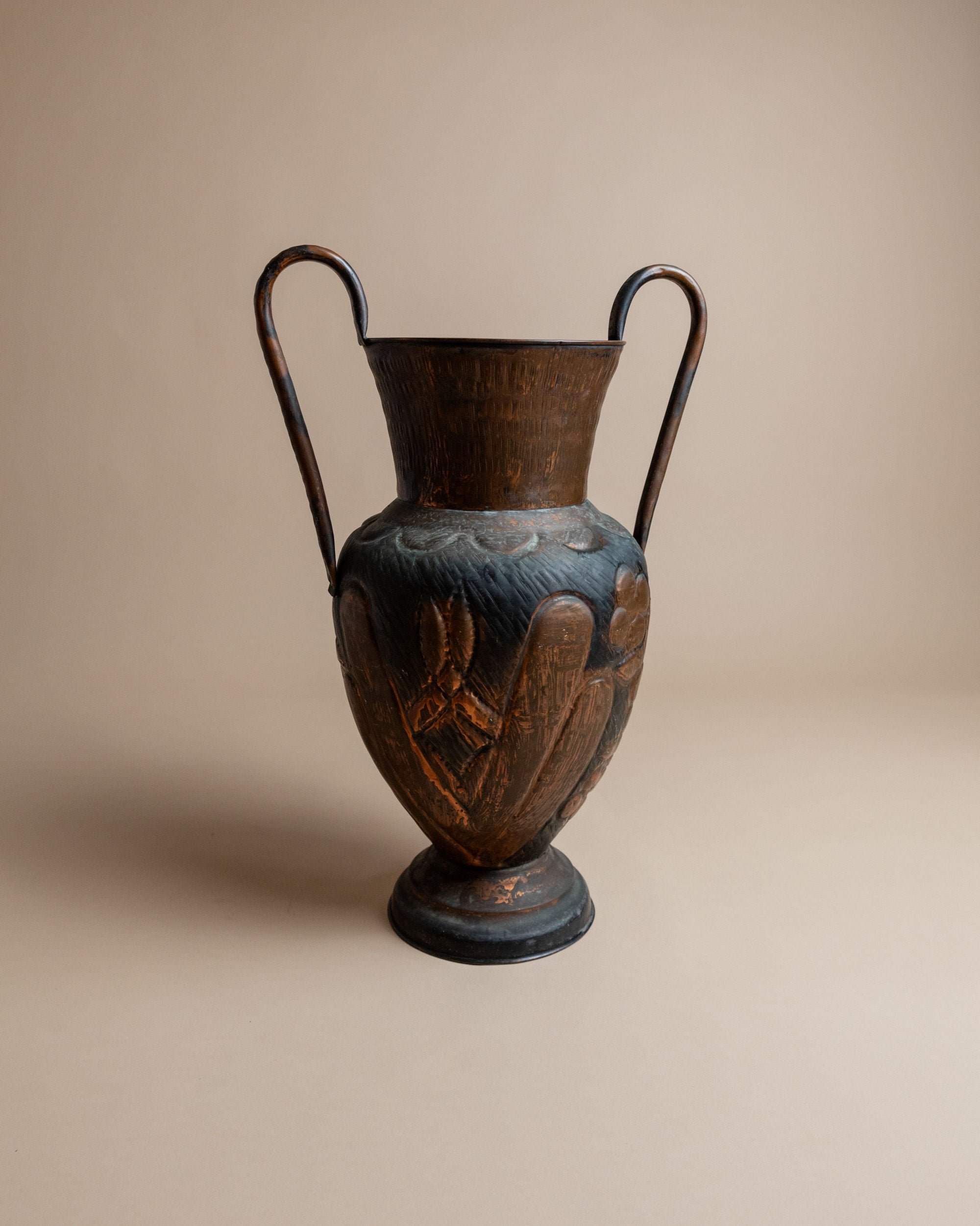 A tall, dark brown ceramic vase from Bottega Jacobs, labeled as the Copper Vase from Italy in the 1960s, features two curved handles and detailed figure carvings resembling a hand-finished amphora. It stands on a wide circular base against a plain beige background.
