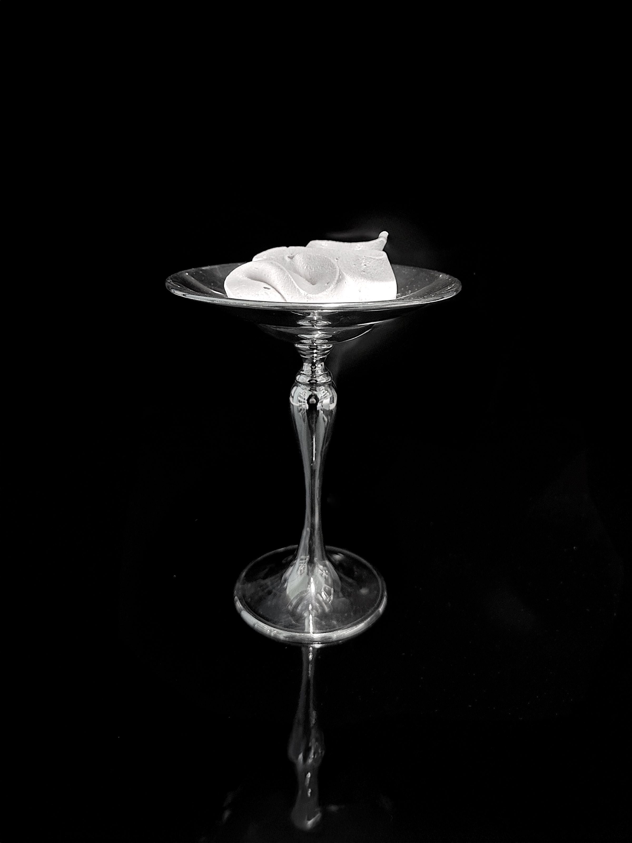 A single, elegant Heavy Silver-Plated Foot Bowl by Dodo Vintage from the 1980s holds a white calla lily bloom, set against a black background with a subtle reflection.