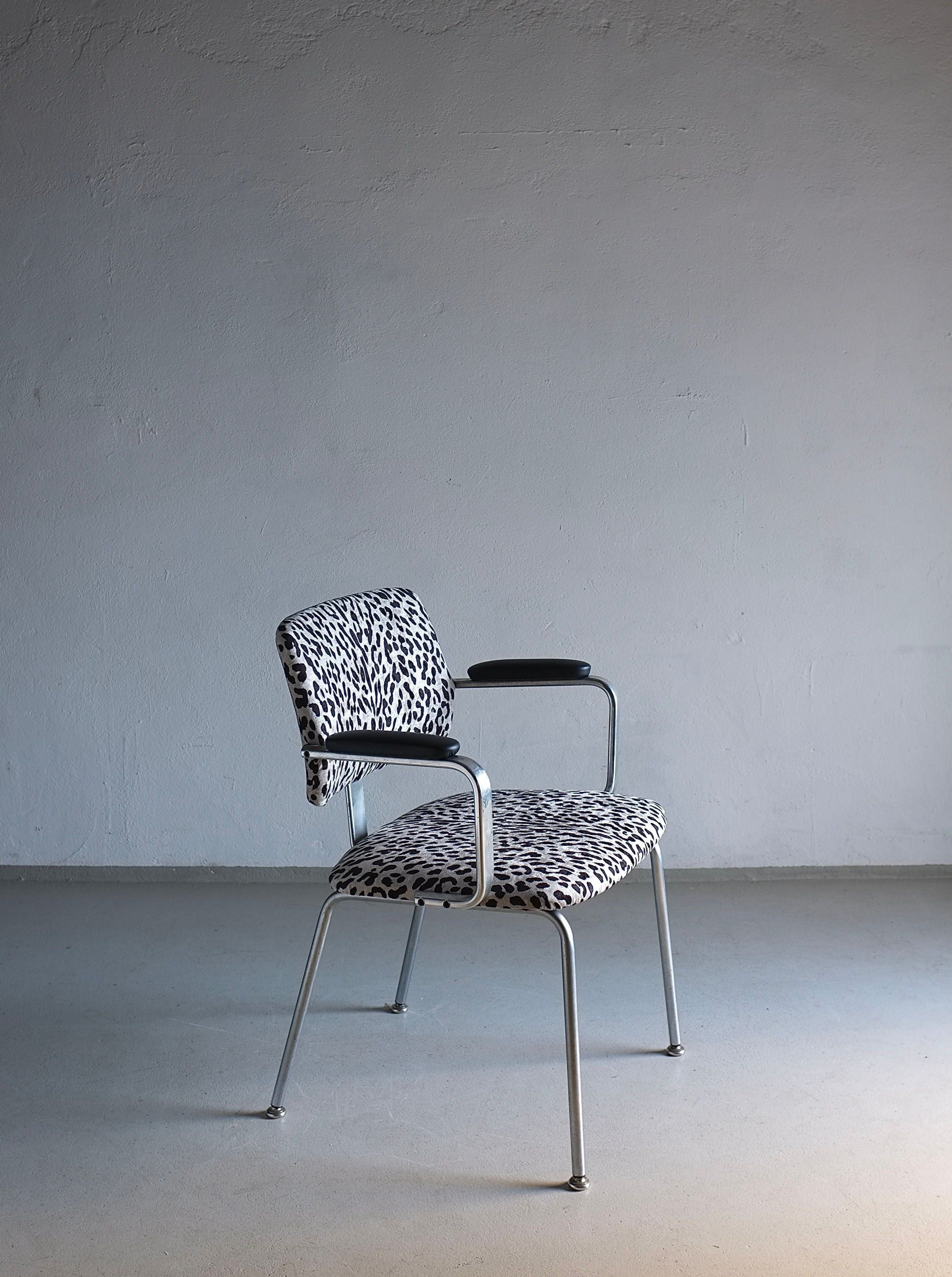 A modern chair with a sleek metal frame and patterned upholstery sits in front of a plain light gray wall. The seat and backrest are covered in black and white animal print fabric, while the leather armrests are black. The Minimalist Animal Print Chrome Desk Arm Chair | Sweden | 1960s by Veter Vintage, reminiscent of a vintage desk chair, is in good vintage condition.
