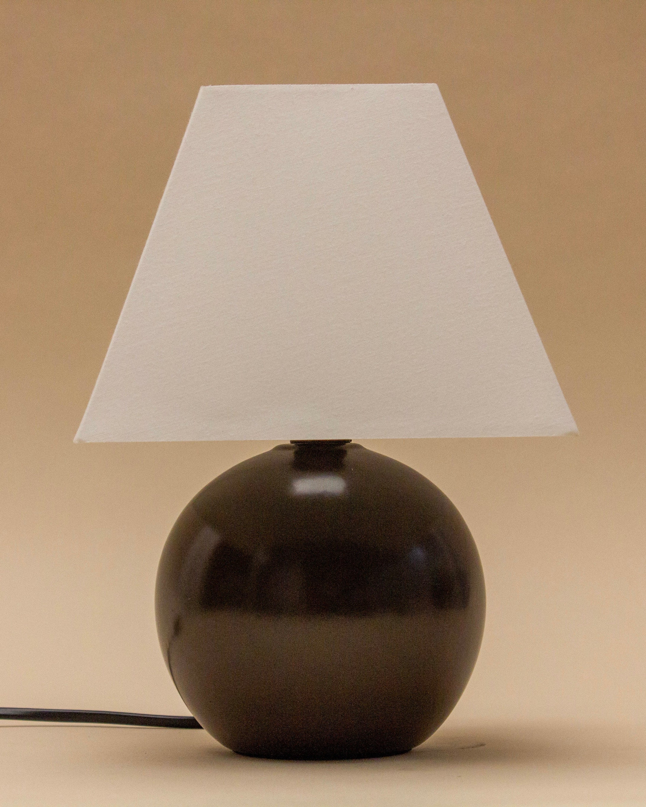 The SÒLER RONDA TABLE LAMP features a round wooden base and a white cone-shaped shade, shown against a beige background with its black power cord visible on the left.