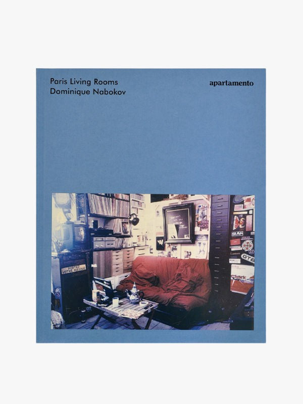 The image shows the cover of the book "Paris Living Rooms by Dominique Nabokov," published by Maison Plage. The cover features a photograph of a cozy living room with a red sofa, bookshelves, and various decorations, capturing Parisian elegance through its eclectic atmosphere.