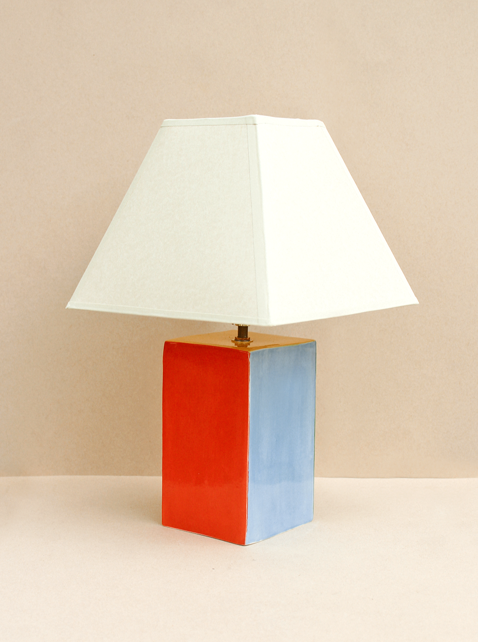 The Paloma Lamp by Casa Veronica features a hand-built ceramic square base—red on one side, blue on the other—and a custom white square lampshade, all set against a neutral beige background.