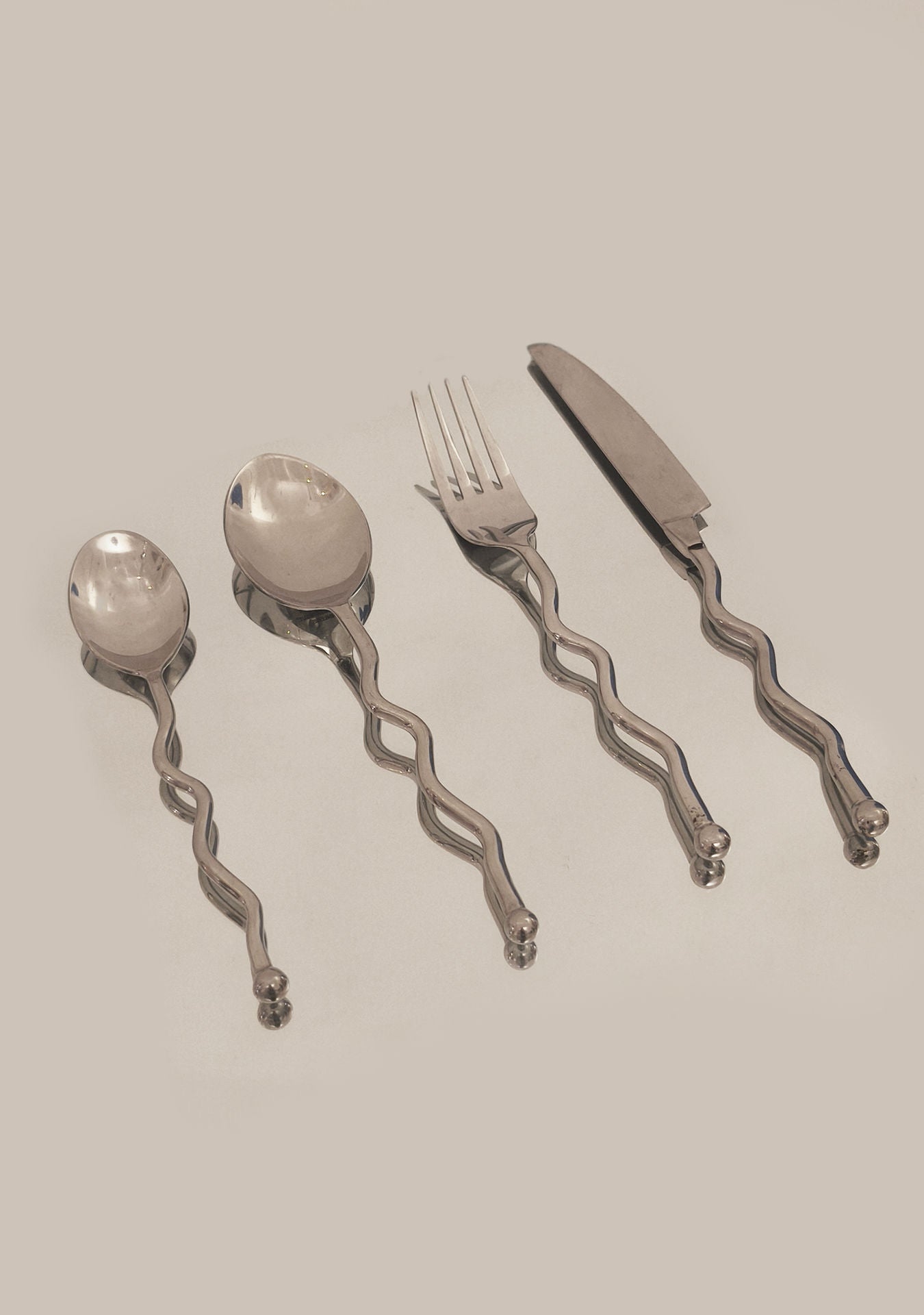 The Les Objoies Set of 4 Zig-zag Cutlery includes a spoon, soup spoon, fork, and knife with wavy twisted handles, arranged side by side on a plain light surface.