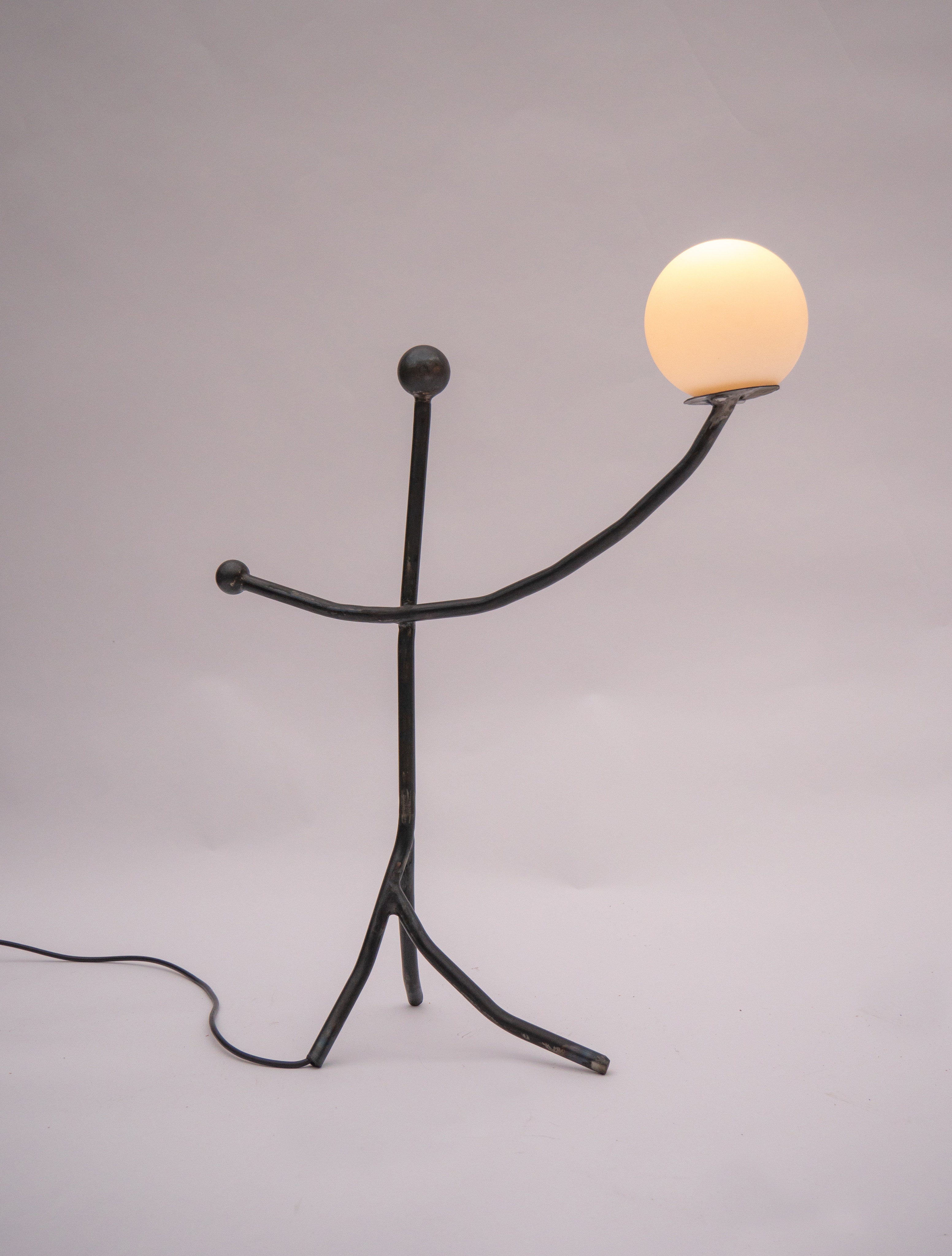 Balancing Act table lamp with sculptural black metal figure holding glowing orb