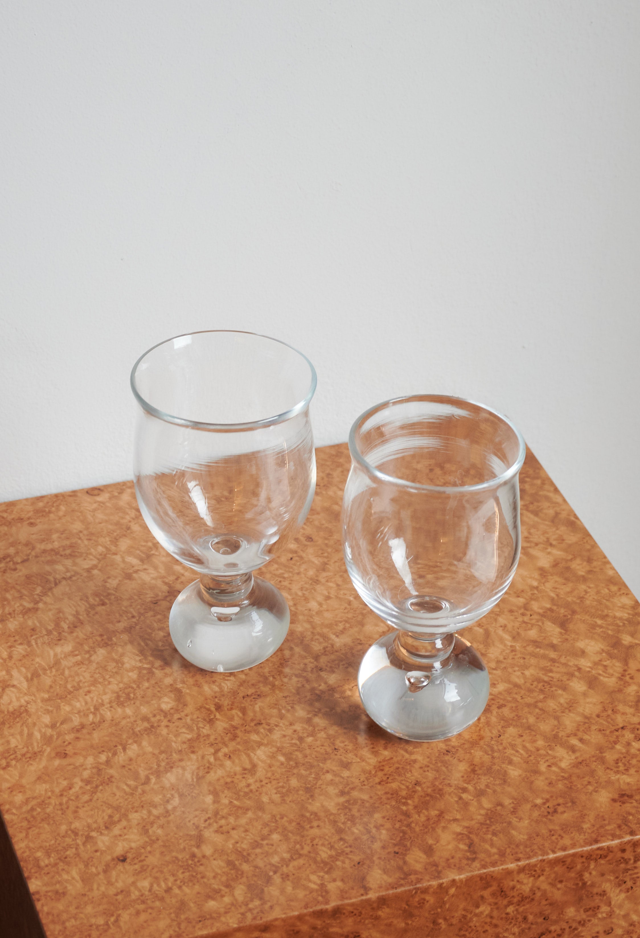 Two clear glass wine goblets with rounded bowls and stems on cork surface