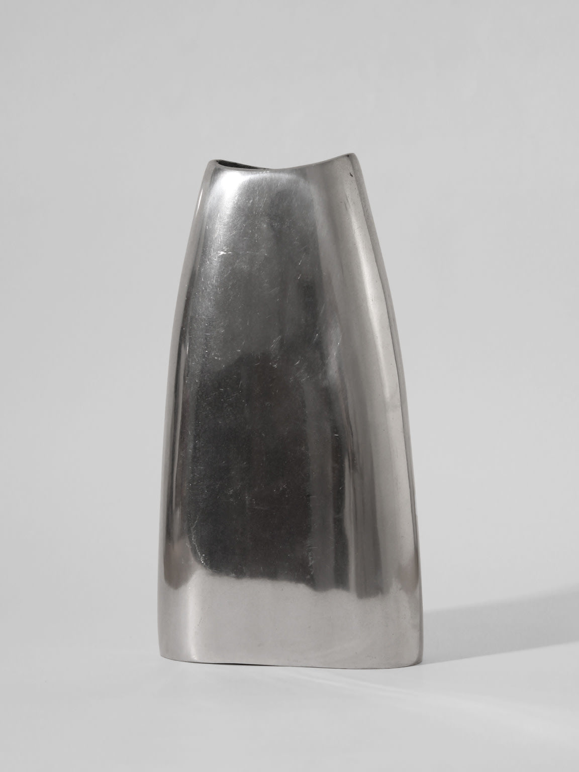 The Polished Aluminum Flat Tall Vase by Vintage Stories features a minimalist, silver finish and sleek asymmetrical design from 1960s Germany, shown against a plain light gray background.