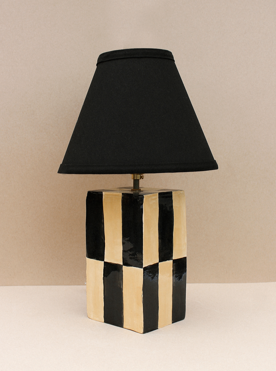 The Casa Veronica Socorro Lamp features a black and beige checkered cubic base with a large black conical shade, adding a sculptural touch against a neutral backdrop.