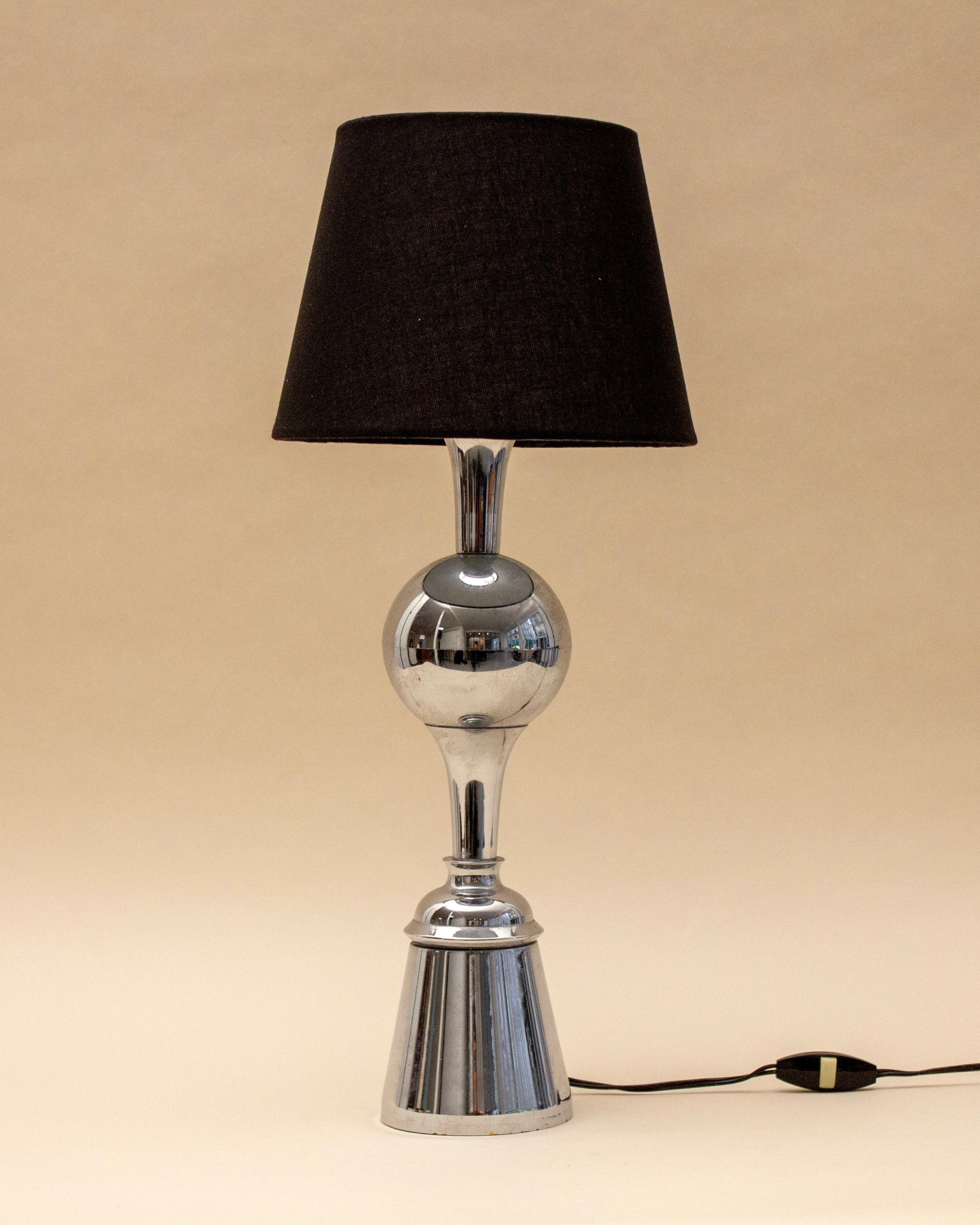 The SÒLER ALBUFEIRA BLACK LAMP features a shiny metal base with a round center detail and a black lampshade. The lamp, switched off, stands against a plain beige background.