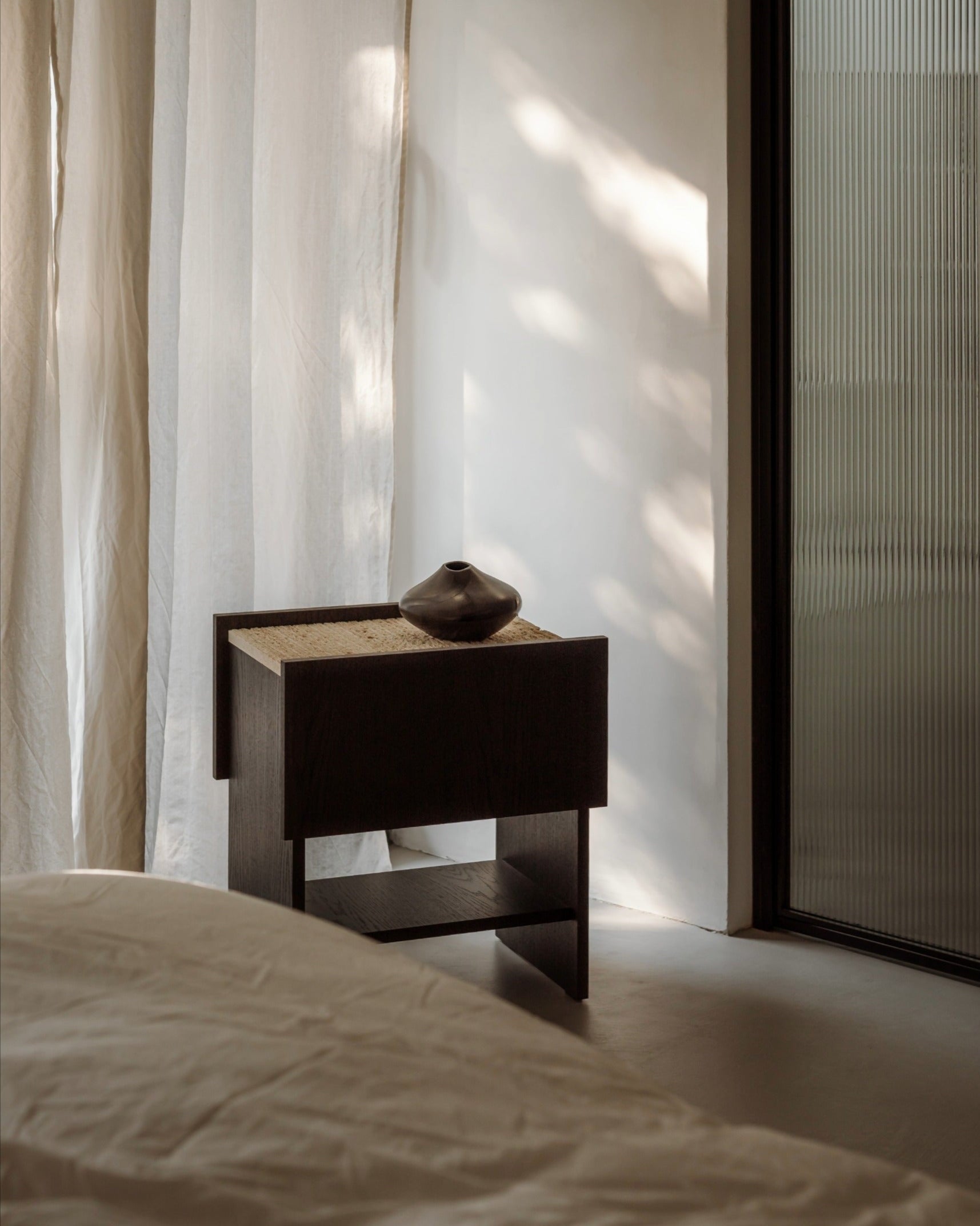 NOTO dark wood nightstand with woven cane top and ceramic vase