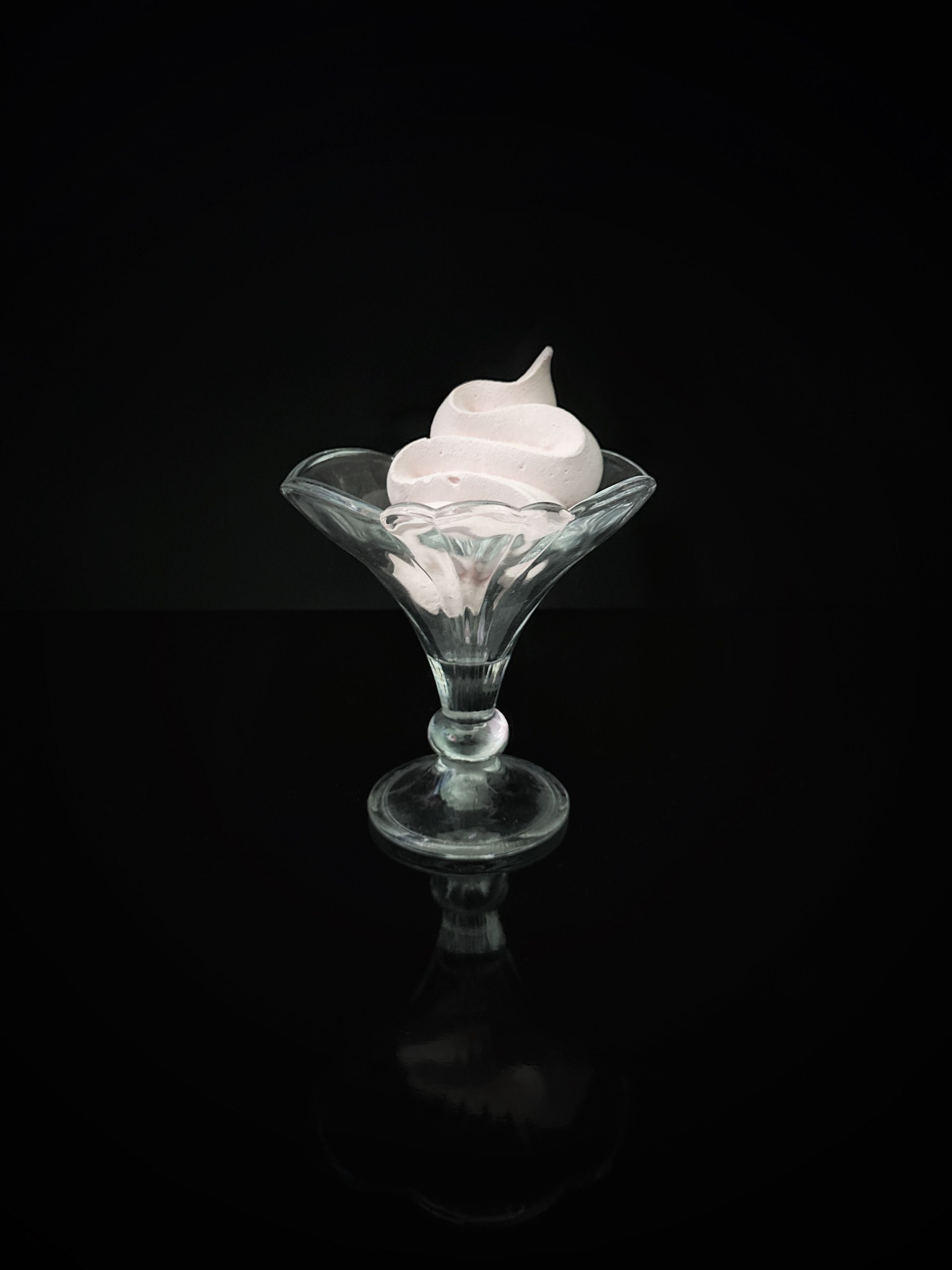 Clear glass dessert cup with swirled cream on black background