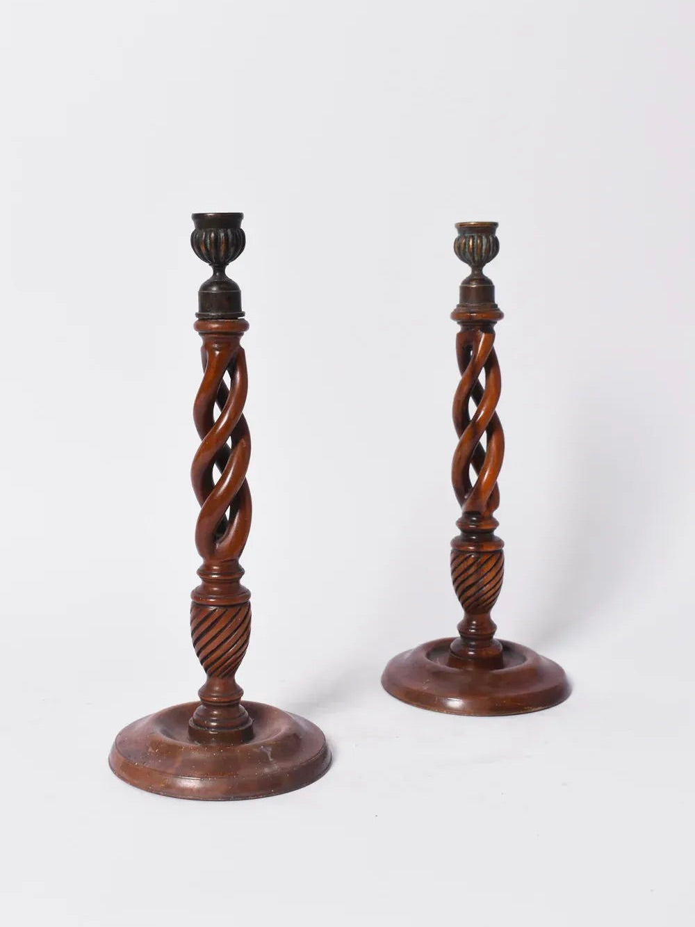 The Barracuda Interiors Pair of Turned Wood Candlesticks, 19th c., features twisted spiral columns, round bases, and dark metal holders, capturing antique charm against a plain white background.